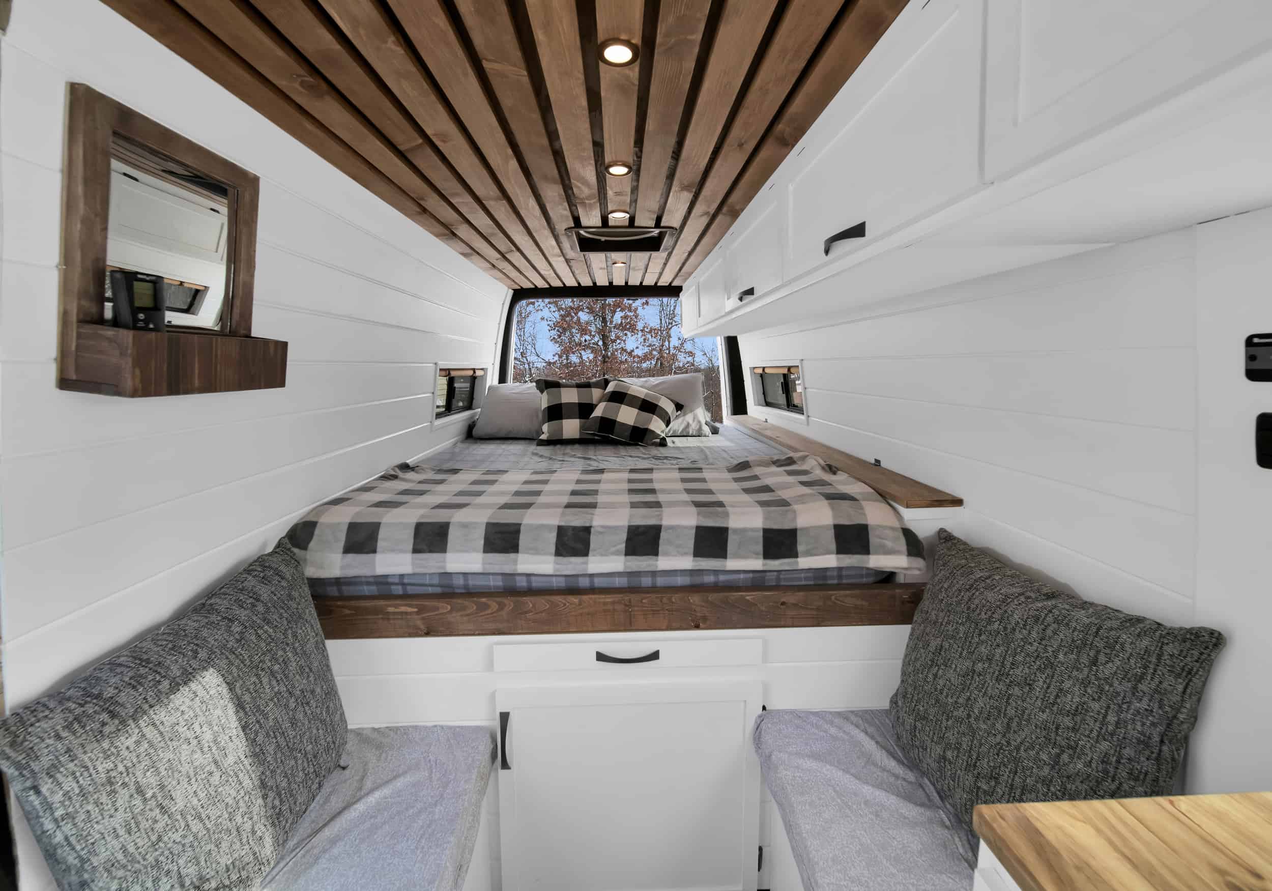 Cozy RV rental bedroom with wooden slat ceiling, white shiplap walls, and a checkered bed. Ideal for van life adventures.. Mercedez Sprinter 2015