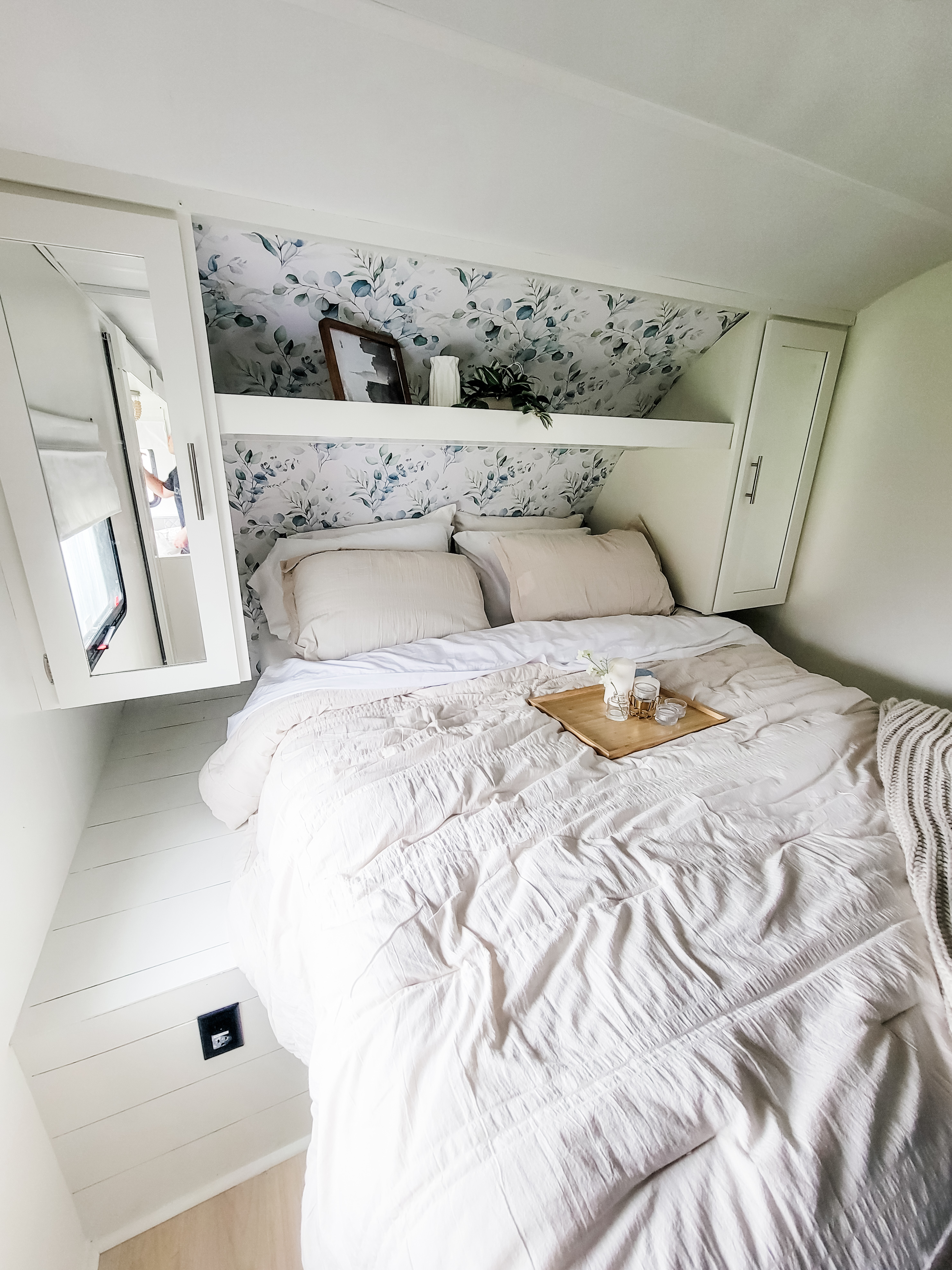 Inside a modern RV rental: a compact, cozy bedroom with beautiful botanical wallpaper, plush bedding, and smart storage.. Forest River Tracer 2022