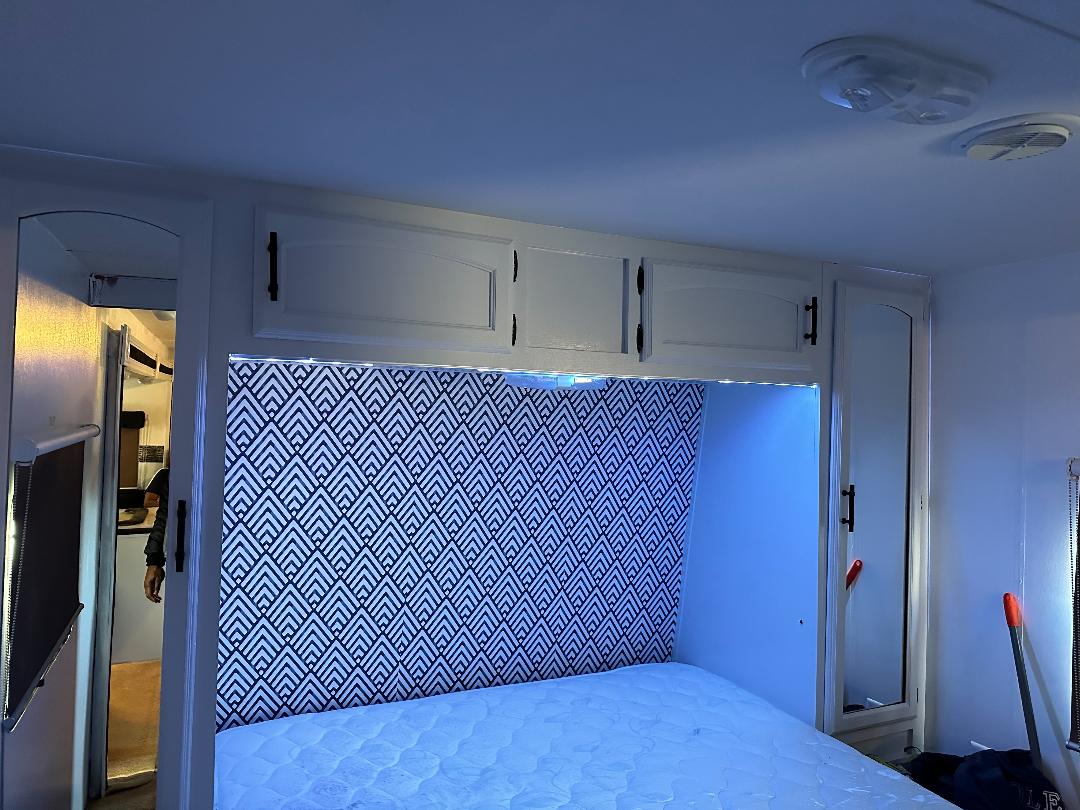 Cozy RV rental bedroom featuring white cabinets, a geometric headboard, and blue LED lighting above the bed.. Forest River Wildwood 2010