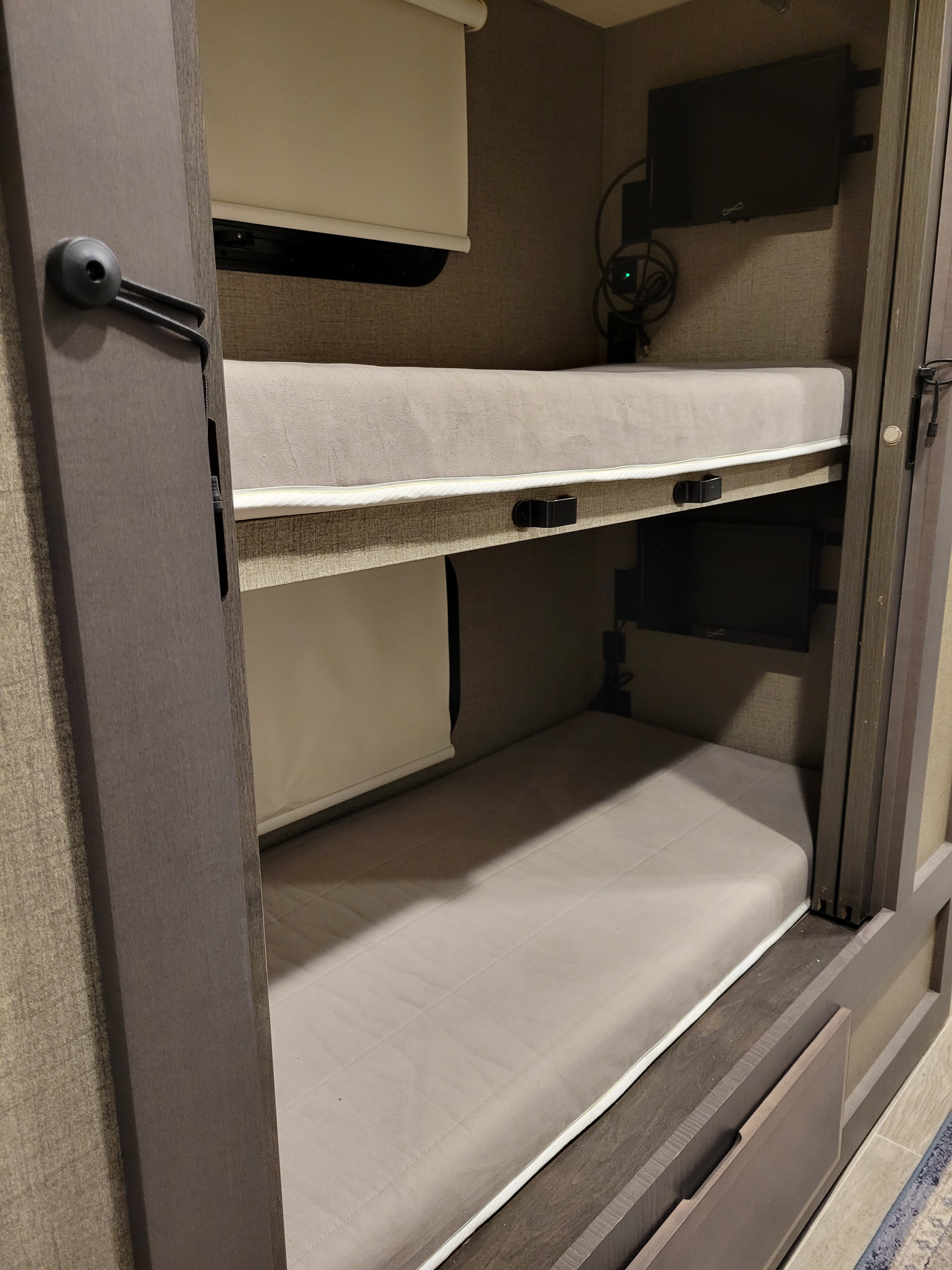 Compact RV rental interior featuring two comfortable bunk beds, each with a mattress, window, and TV for entertainment.. Thor Motor Coach Omni 2022