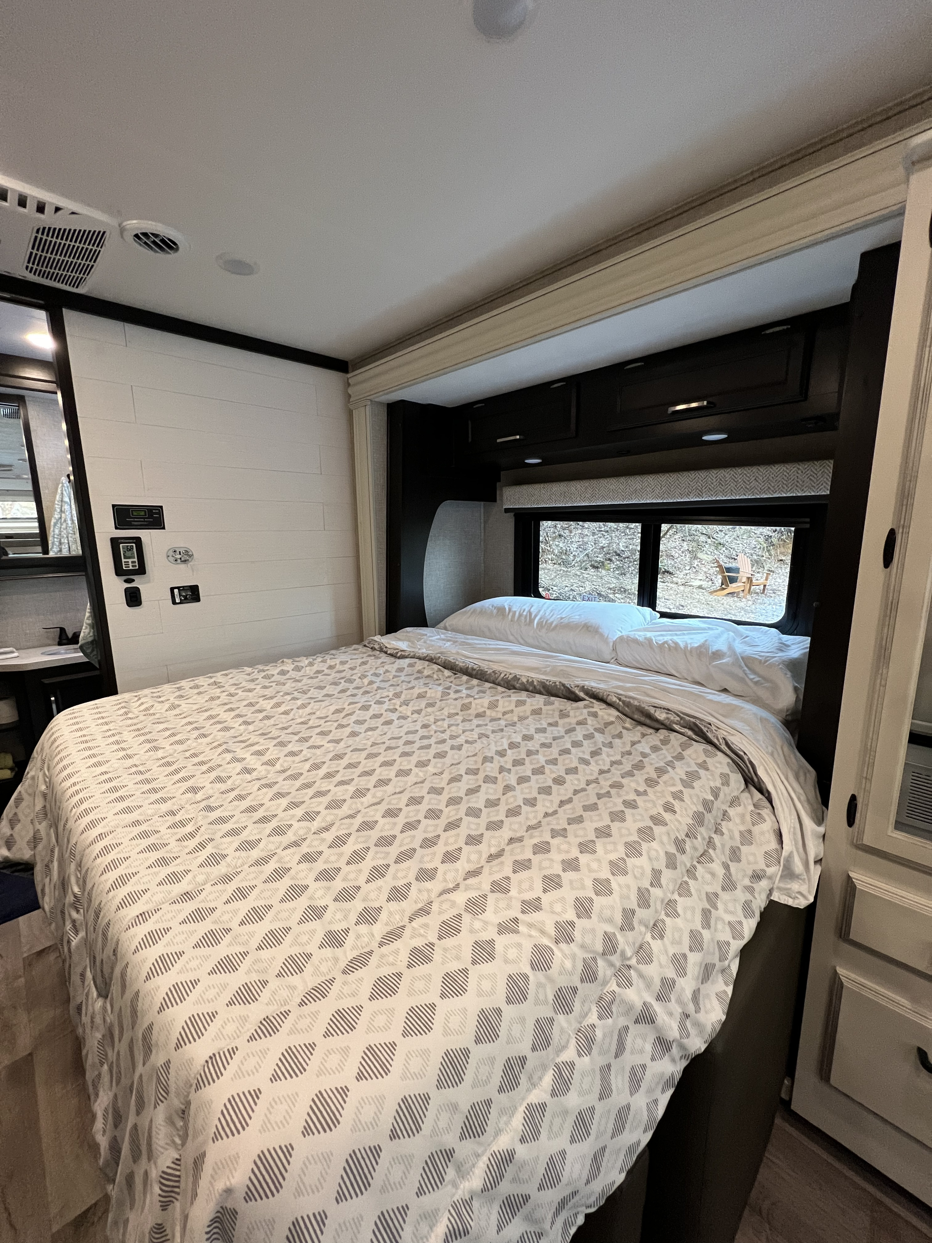 Experience comfort in this RV rental bedroom. Features patterned bedding, overhead storage, and a scenic window view.. Entegra Coach Odyssey 2023