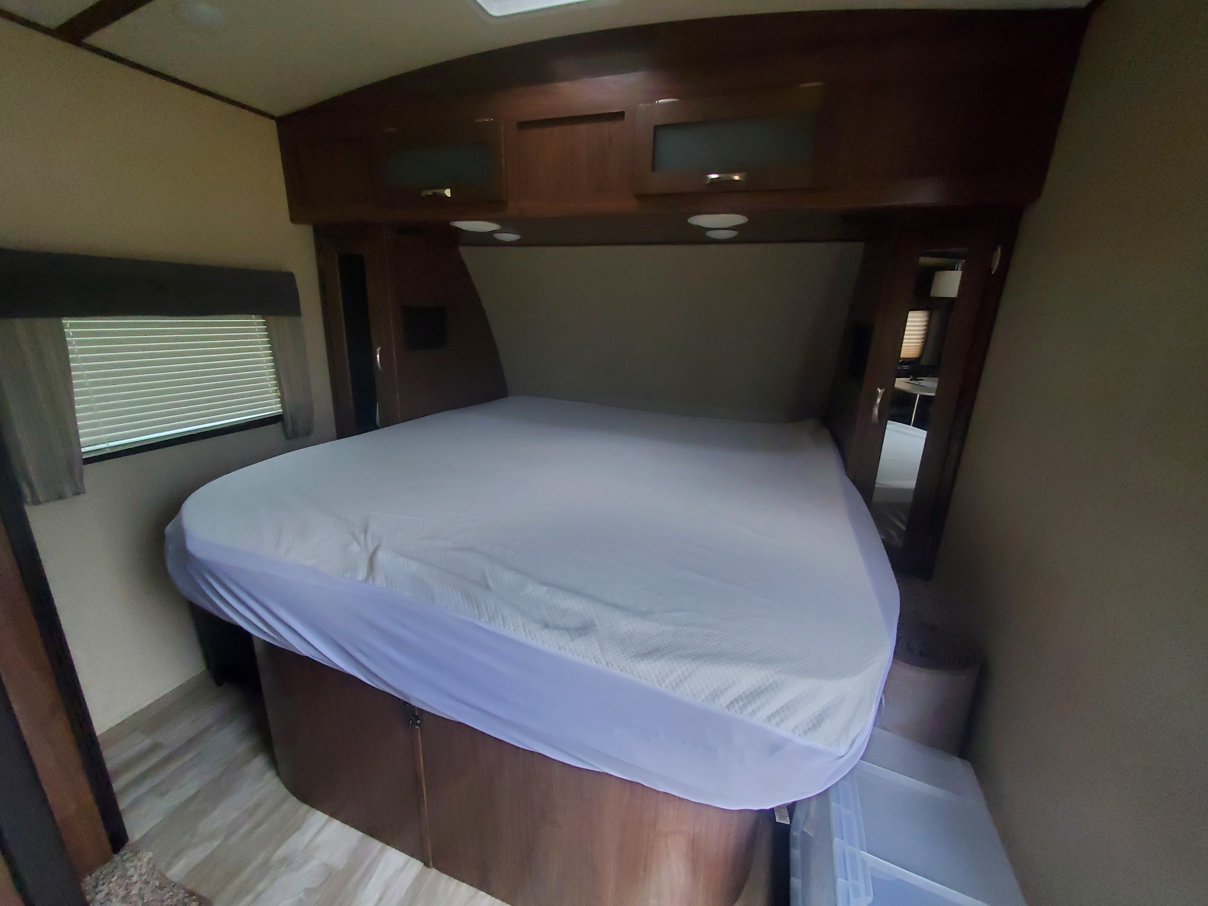 RV rental bedroom: Features a large white-covered bed, dark wood overhead cabinets, and a window with blinds.. Dutchmen Aerolite 2017