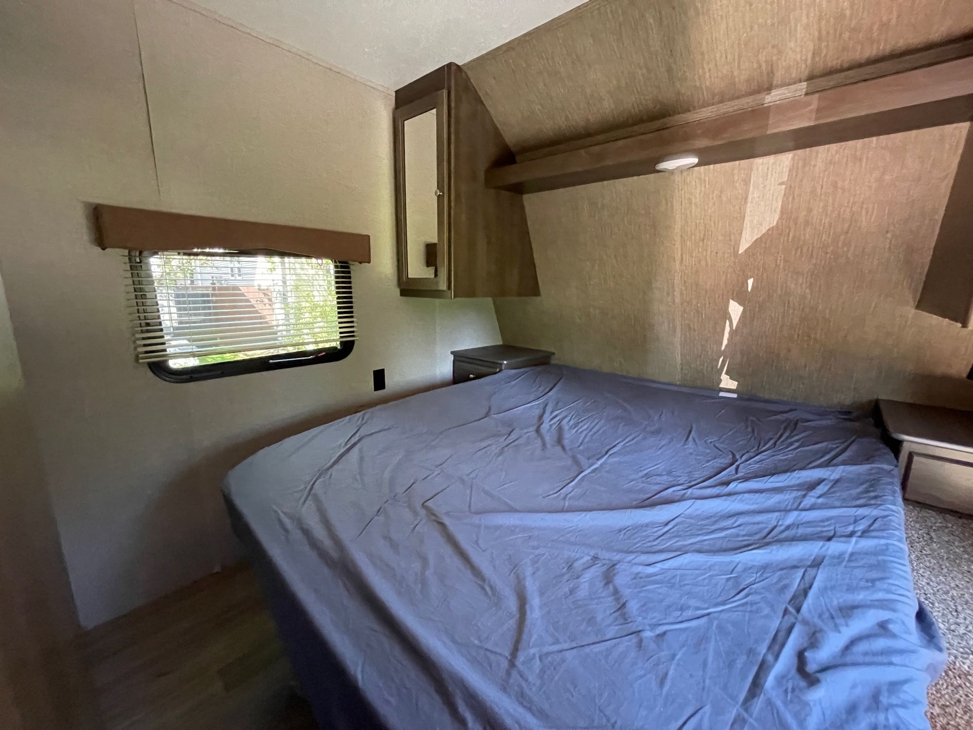 Inside an RV rental, a compact bedroom with a blue-sheeted bed, window with blinds, and built-in storage.. Coleman Lantern 28.6 RK 2018