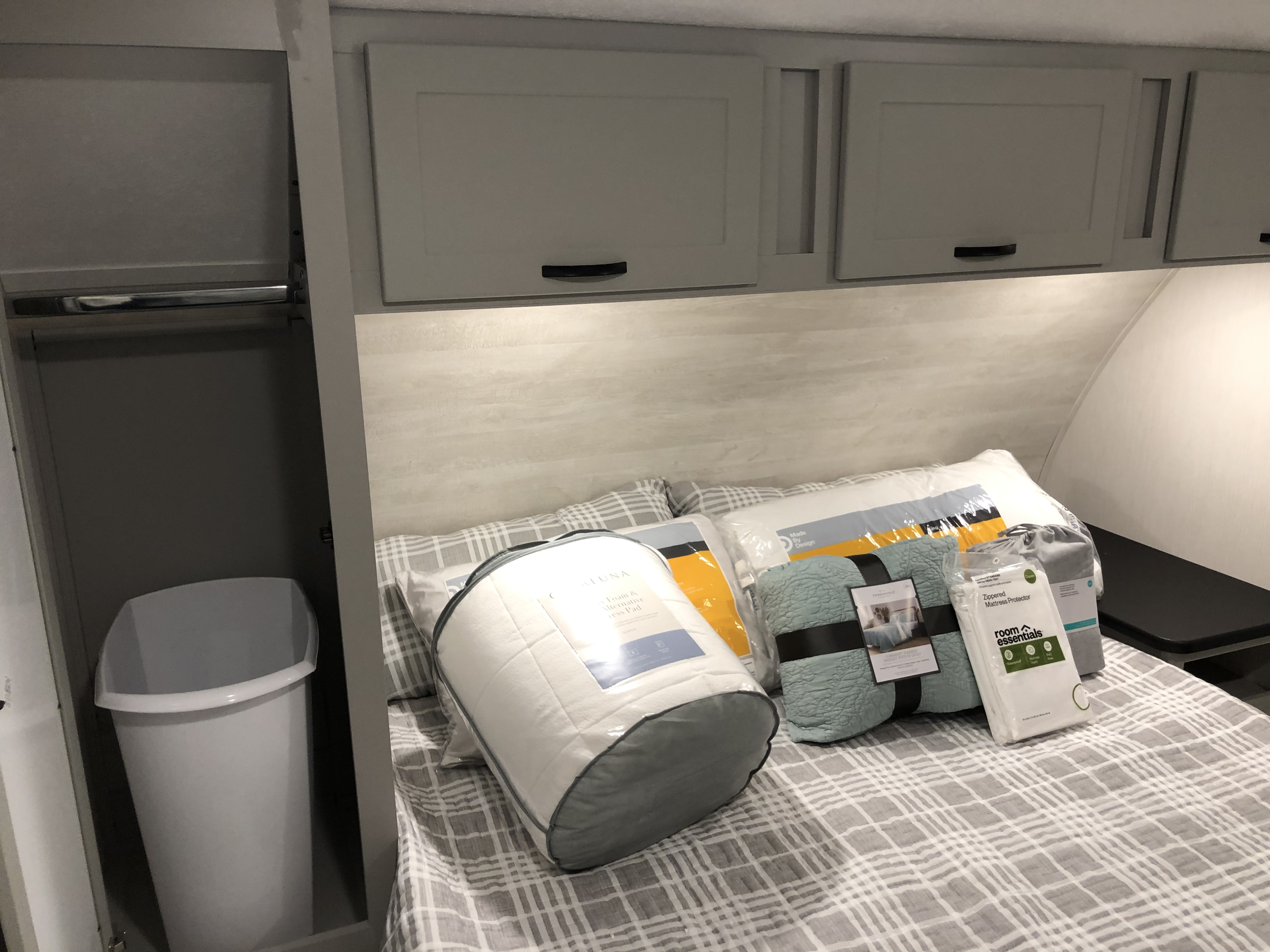 Clean RV rental bedroom showing new bedding on a plaid bed, white overhead cabinets, and a small closet with a trash can.. Forest River Vibe 2022