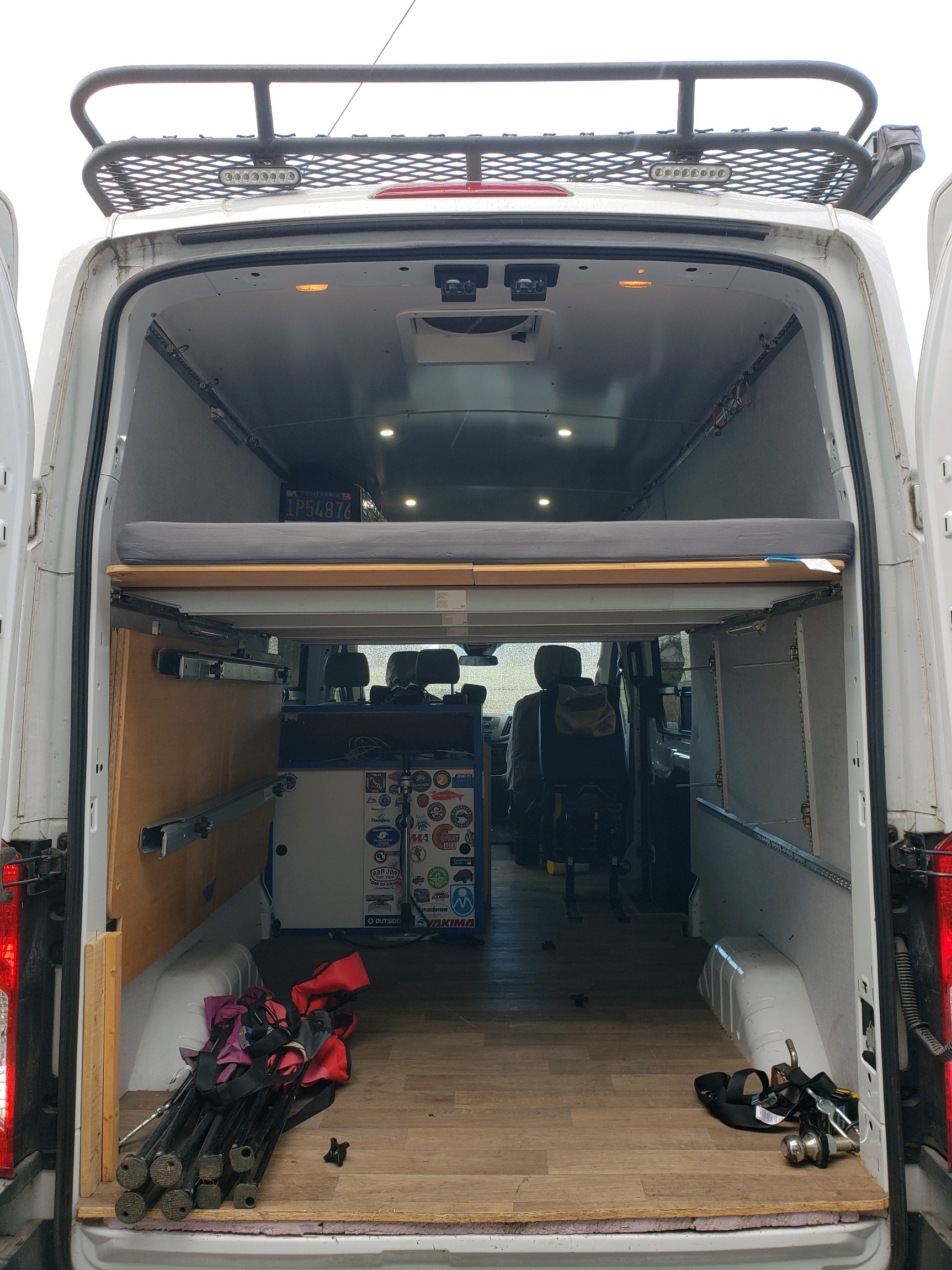 Open rear doors reveal a camper van's interior: bed, storage, wood floor. Great for an rv rental road trip or adventure.. Ford Transit 2016