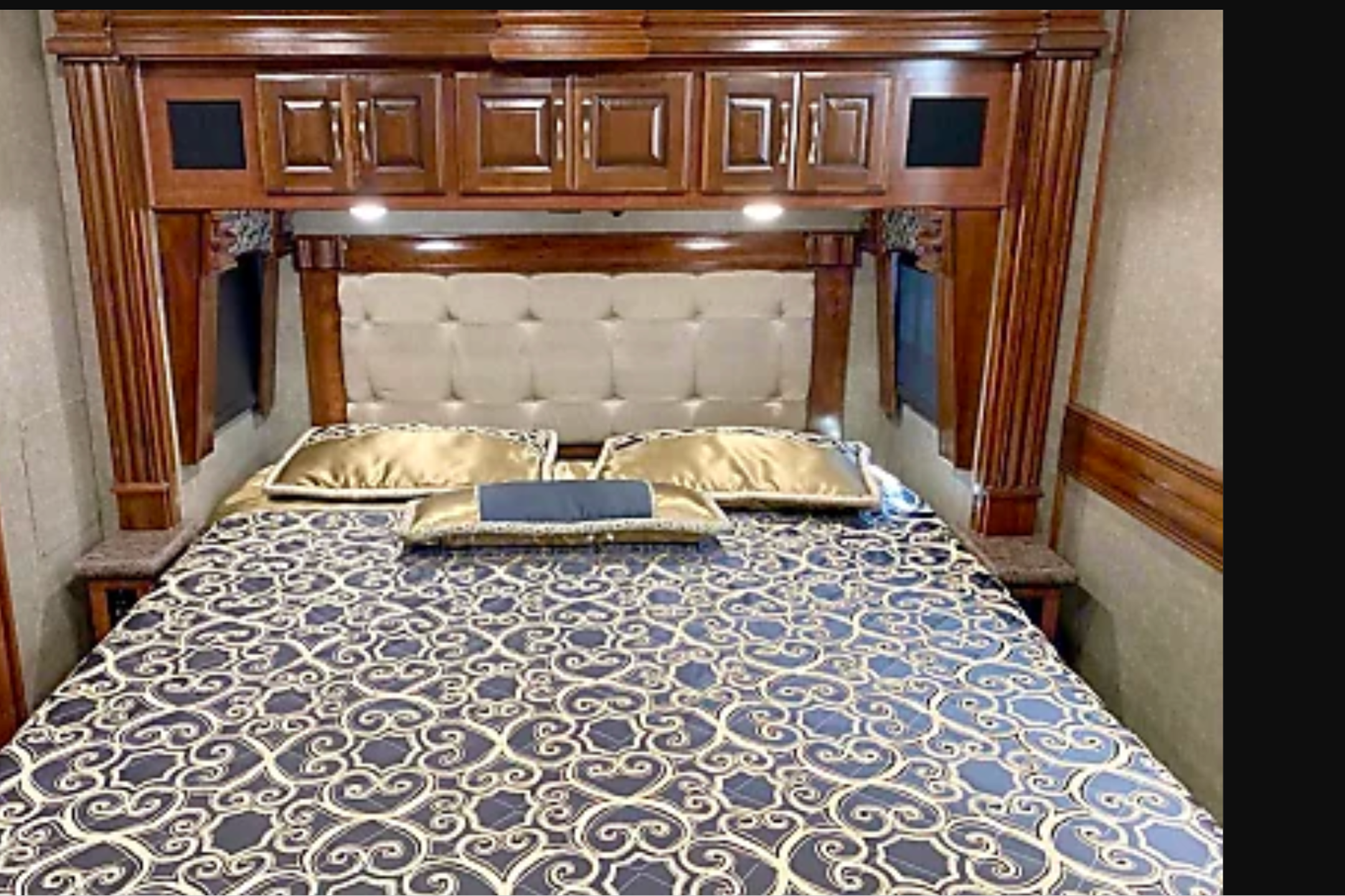 Step into comfort with this RV rental bedroom, featuring a tufted headboard, built-in storage, and patterned bedding.. Fleetwood Discovery 2019