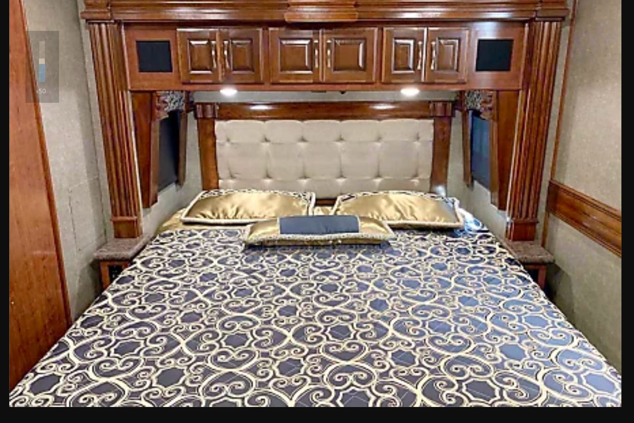 Cozy RV rental bedroom with a large bed, patterned bedding, tufted headboard, and ornate wood overhead cabinets.. Fleetwood Discovery 2019
