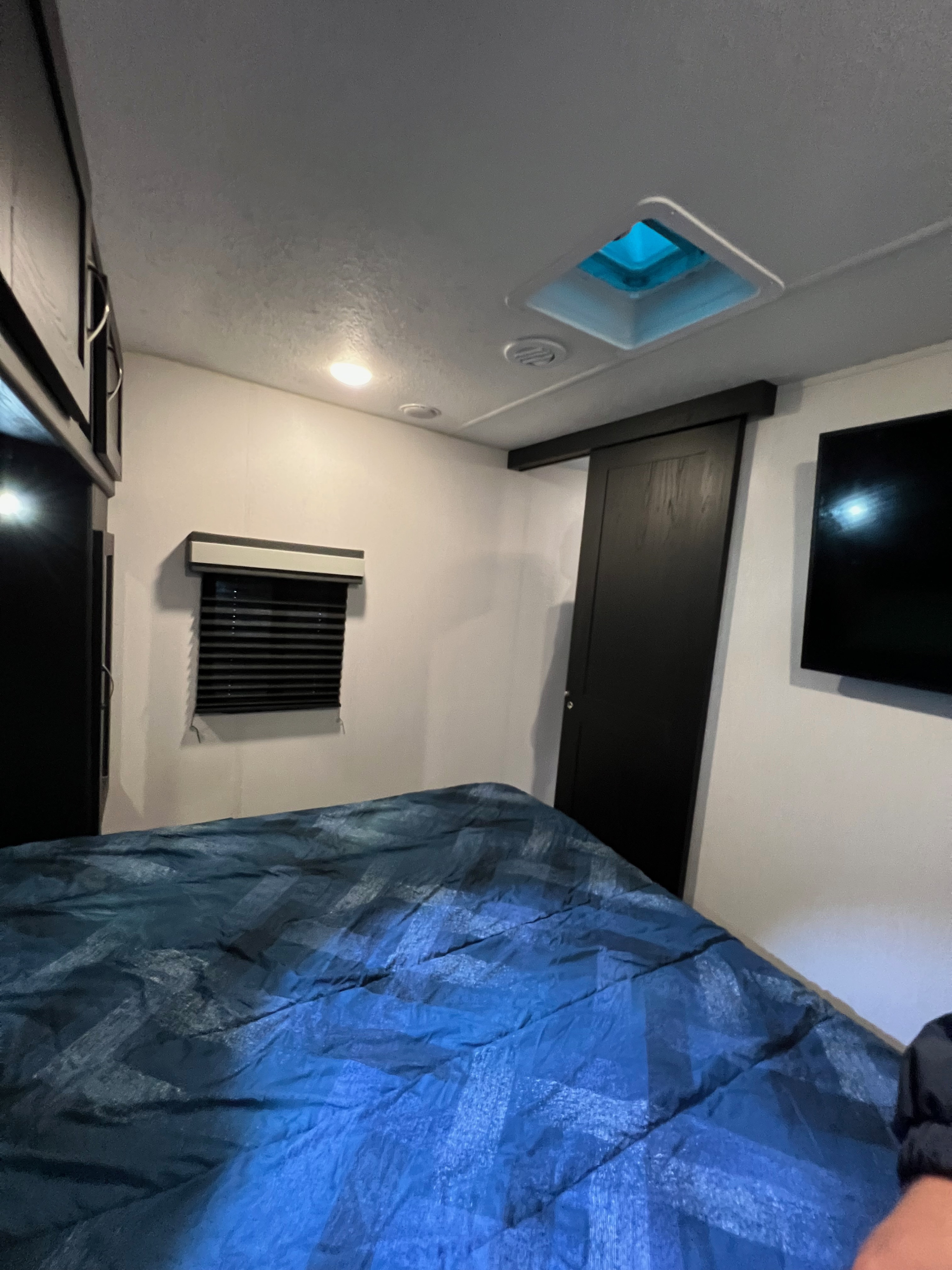 Inside an RV rental bedroom: blue bed, overhead storage, window blinds, TV, and ceiling vent. Bright and functional.. Coachmen Freedom Express 2022