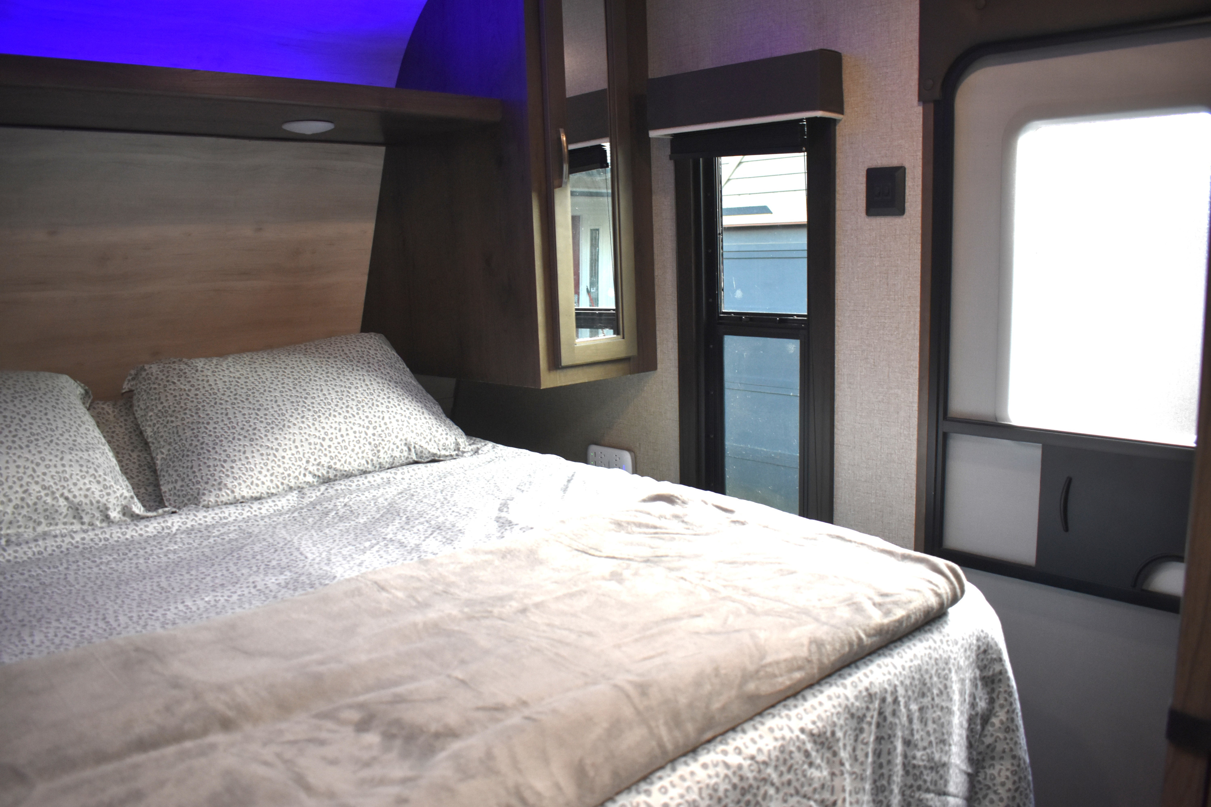 Experience comfort in your RV rental. A modern bedroom features a large bed with patterned linens, ambient blue lighting, and a window.. Jayco Jay Flight SLX Rocky Mountain Edition 2021