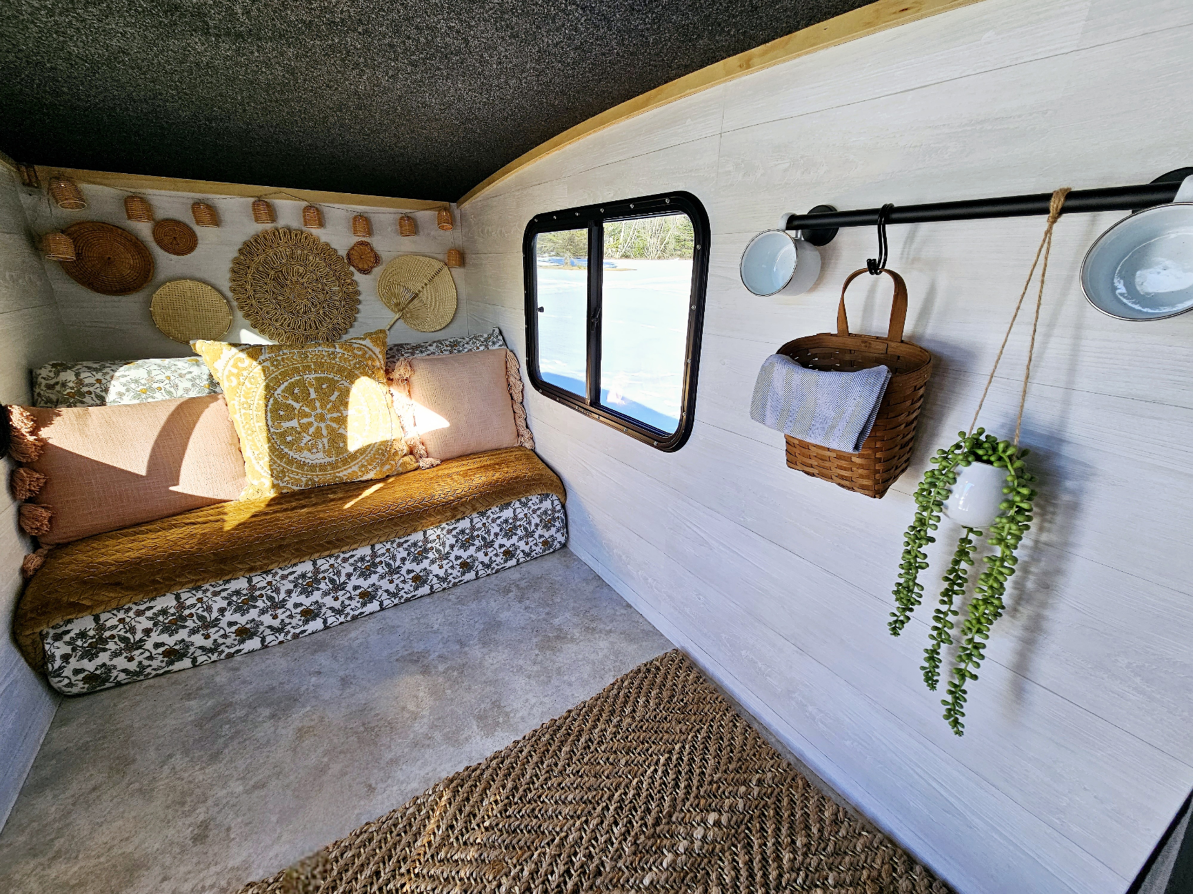 Cozy RV rental interior with a comfy daybed, bohemian decor, a vibrant rug, and a scenic window view.. Runaway Coolcamp-XL 2018