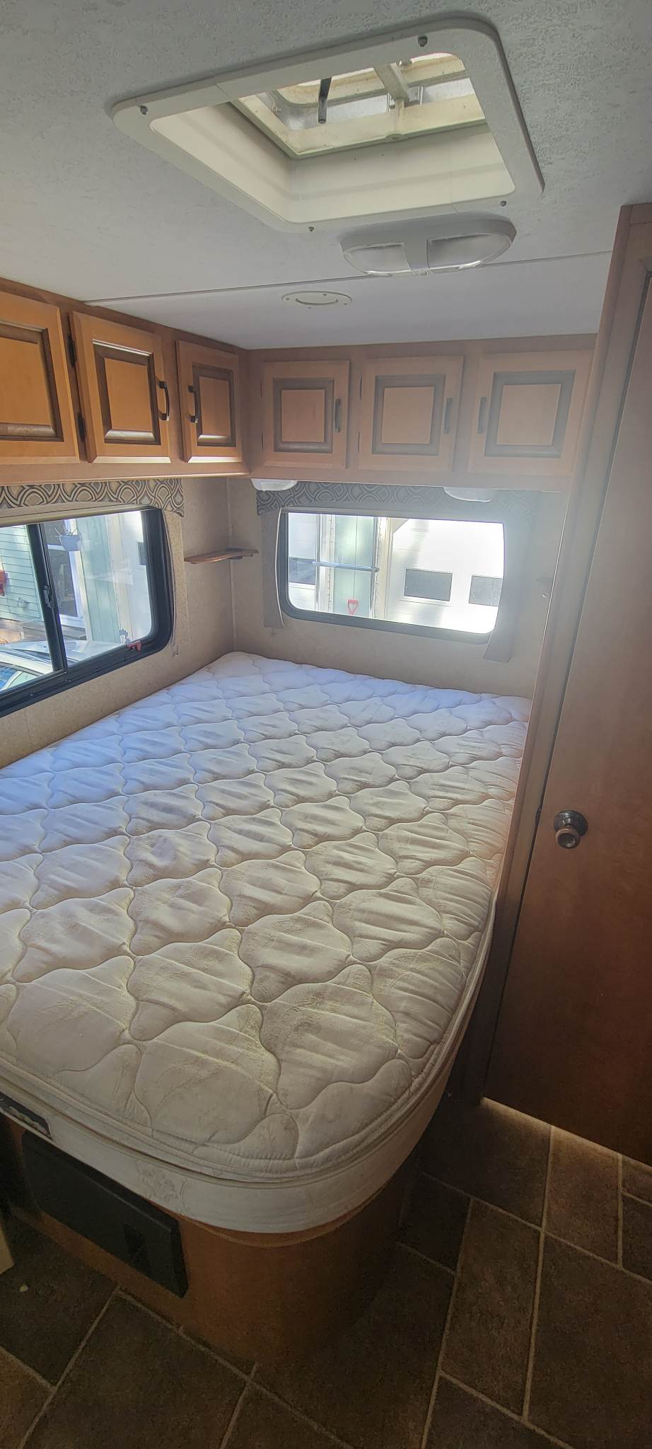 Compact RV rental bedroom with a cozy mattress, convenient overhead cabinets, and two windows for light.. Forest River Sunseeker 2012
