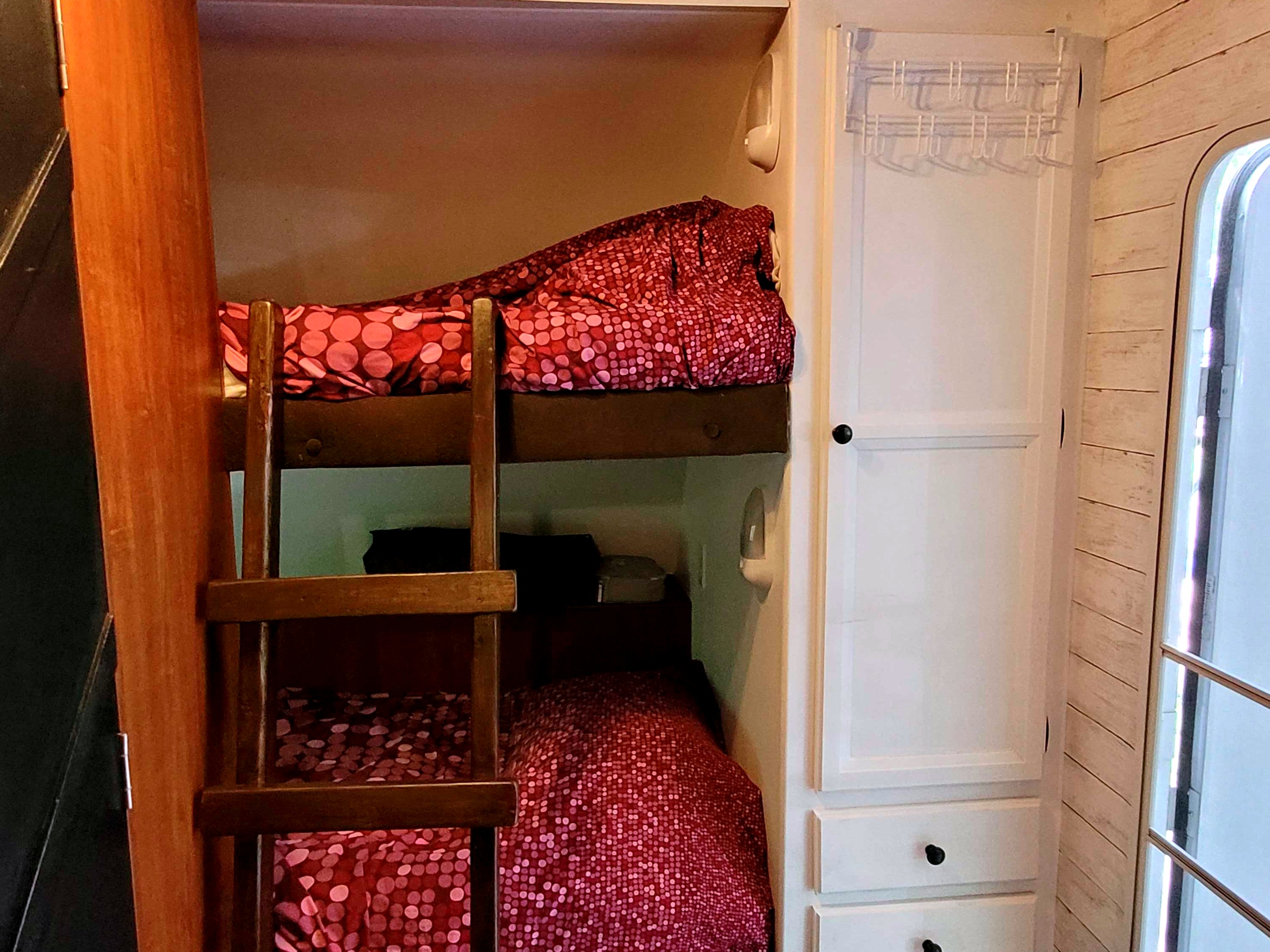 RV rental bedroom featuring built-in bunk beds with red patterned bedding, a wooden ladder, and white storage cabinets.. Jayco X213 2013