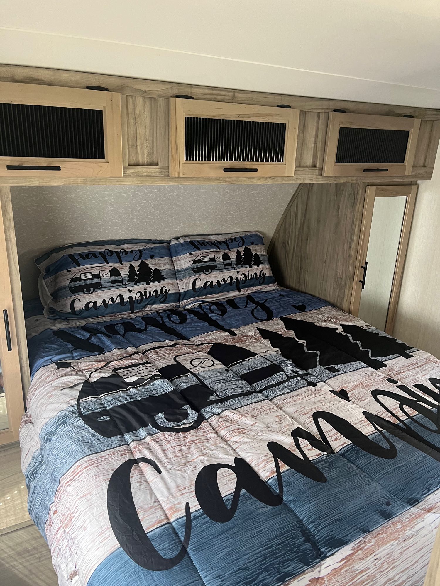 Inside this RV rental's cozy bedroom: Happy Camping bedding, wood cabinets, and a convenient built-in mirror.. Forest River Cherokee Alpha Wolf 2022