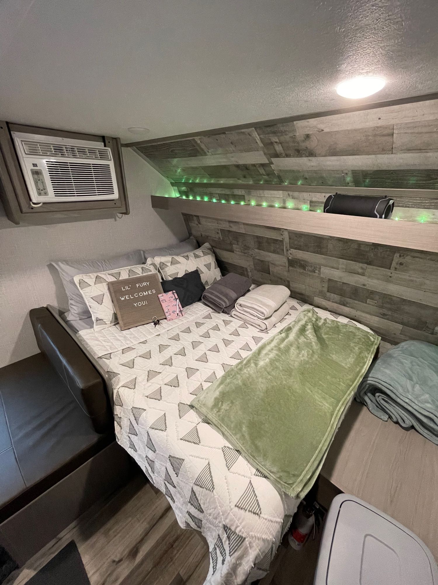 This cozy & compact RV rental bedroom features a comfortable bed, AC unit, and welcoming decor with string lights.. Coleman Lantern 17B 2023
