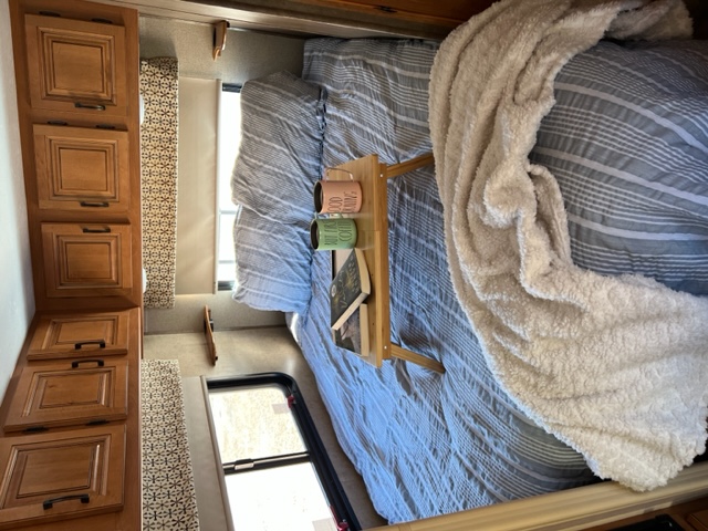 Cozy RV rental bedroom with blue striped bedding, a fluffy white blanket, and a bed tray with coffee mugs and a book.. Forest River Sunseeker 2016