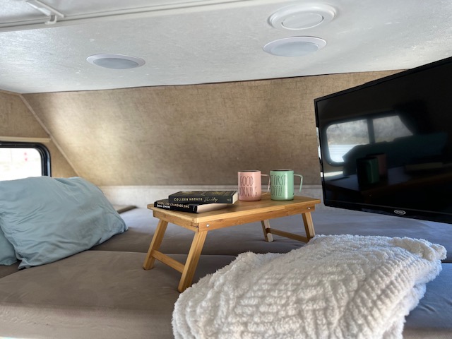 Cozy RV rental interior: bed, TV, and breakfast tray with "GOOD MORNING" coffee mugs and books for a relaxing start.. Forest River Sunseeker 2016