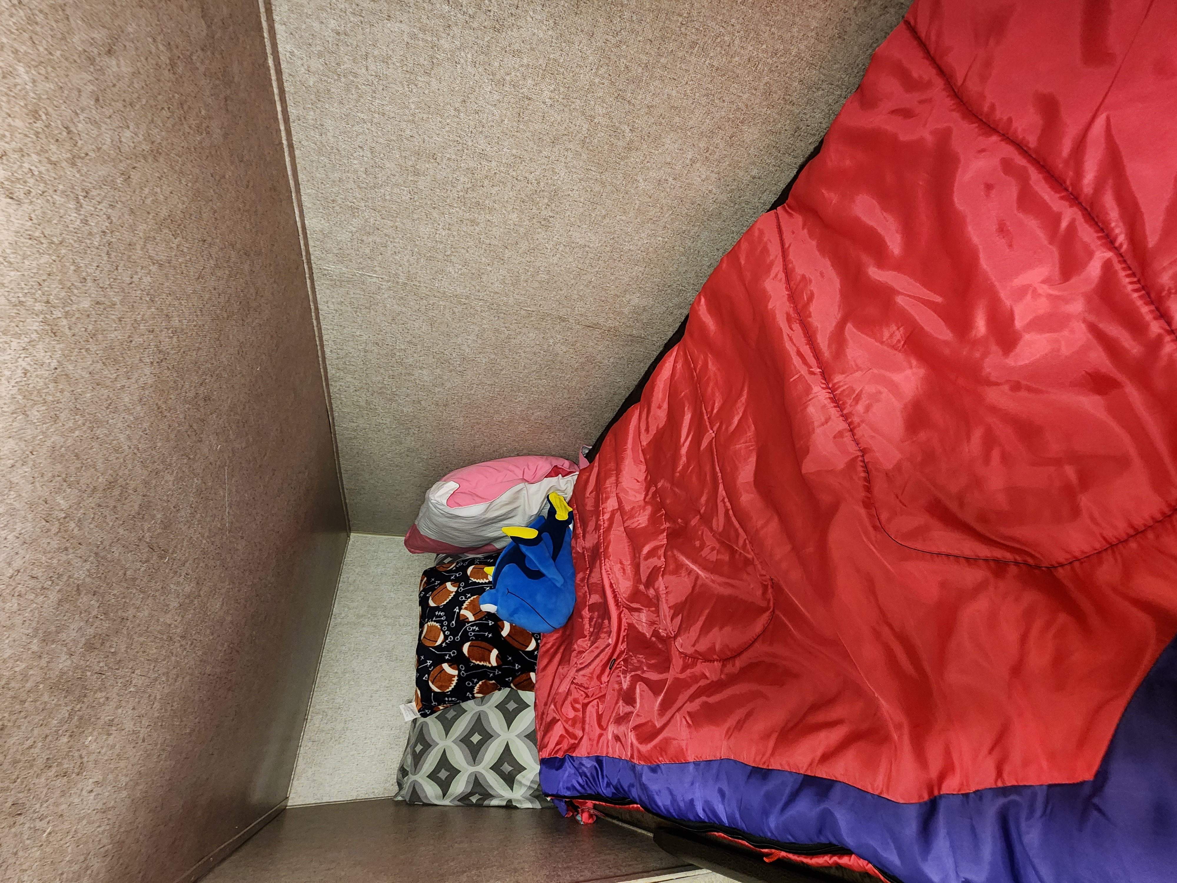 An RV rental sleeping area with a red and purple sleeping bag, Dory plush, and football-patterned blanket in a cozy bunk.. Forest River Coachmen Catalina SBX 2018