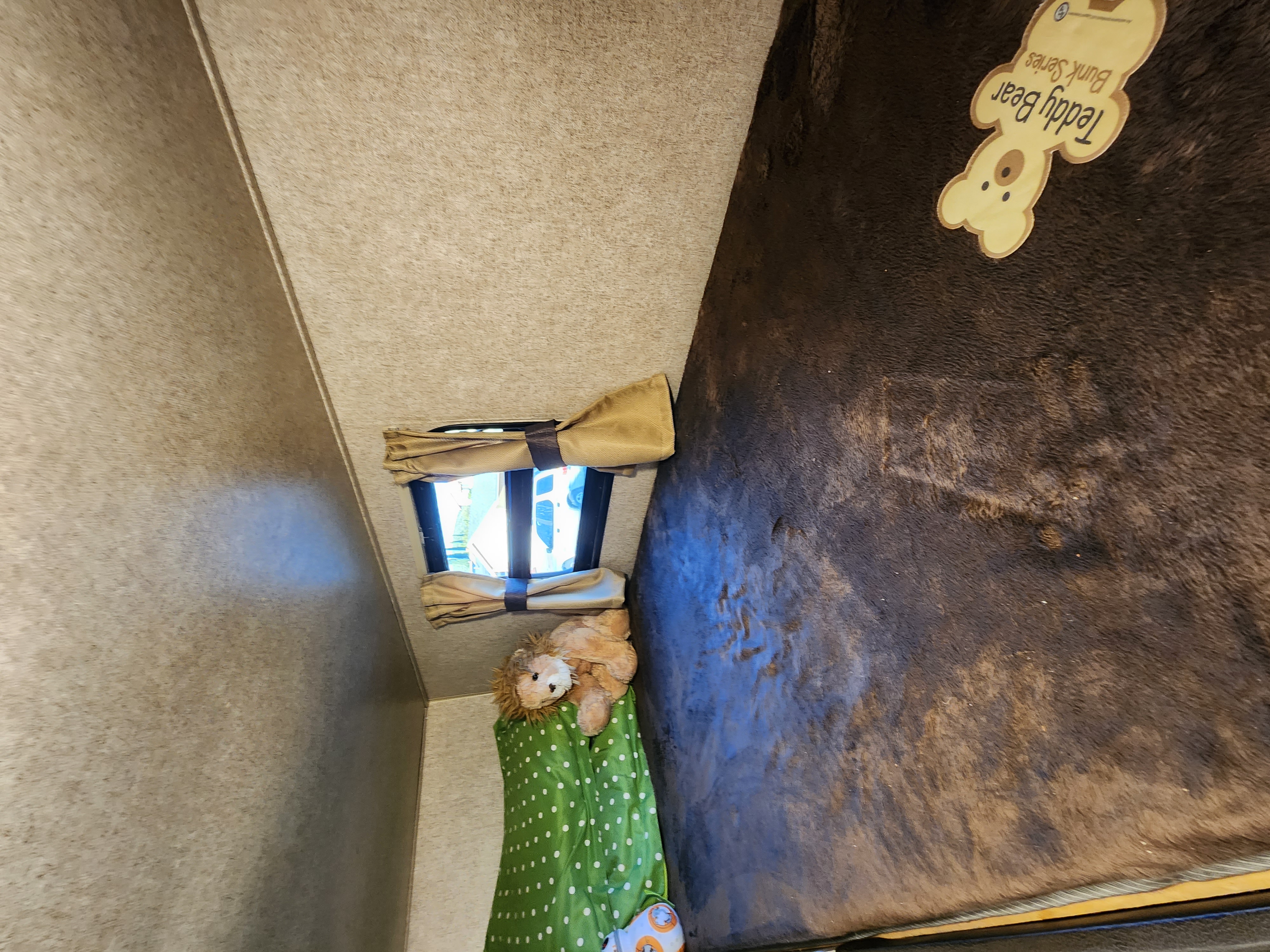 Cozy RV rental bunk with window, dark brown blanket, stuffed lion, and BB-8 droid. Features a "Teddy Bear Bunk Series" label.. Forest River Coachmen Catalina SBX 2018