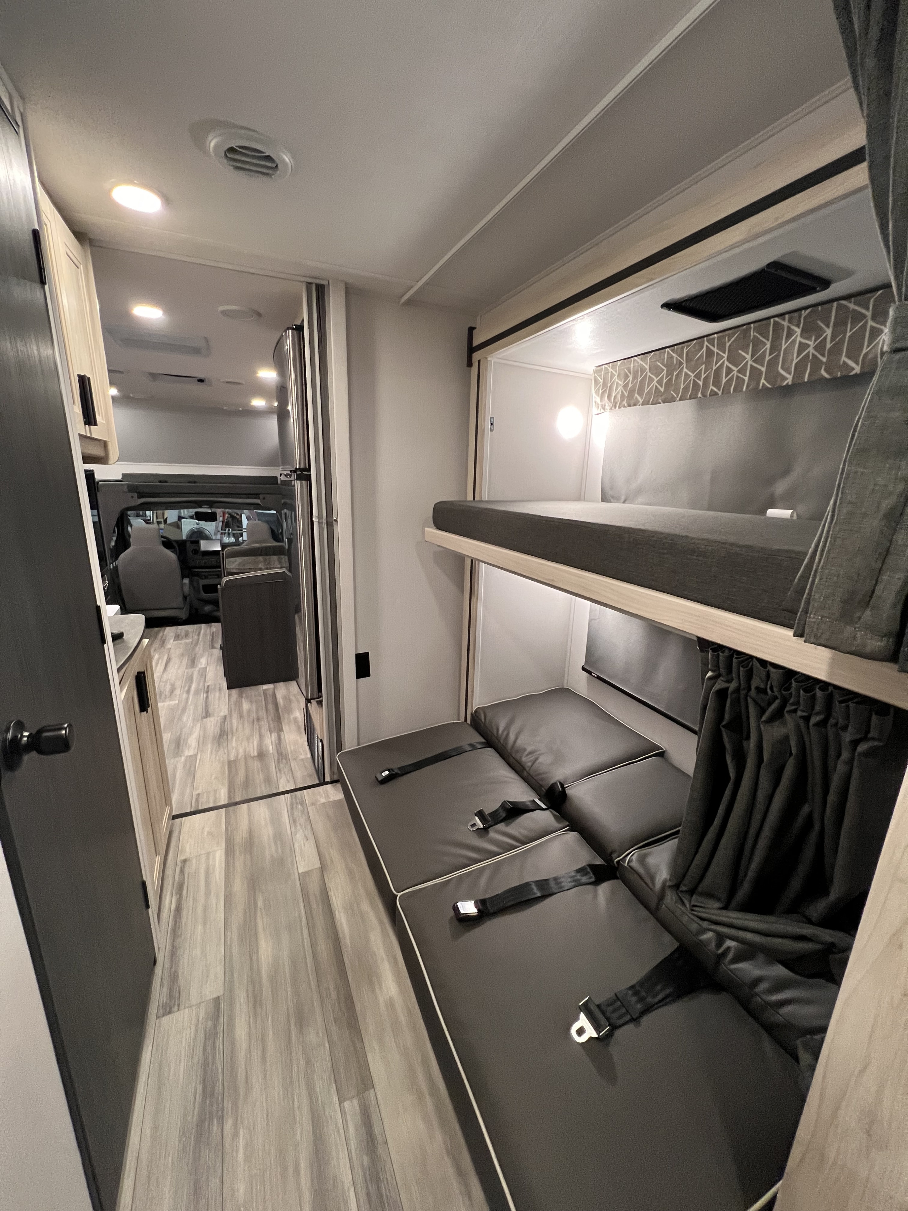 RV rental interior features bunk beds: an upper sleeping area and a lower cushioned bench with seatbelts, leading to the front cabin.. Forest River Sunseeker 2024
