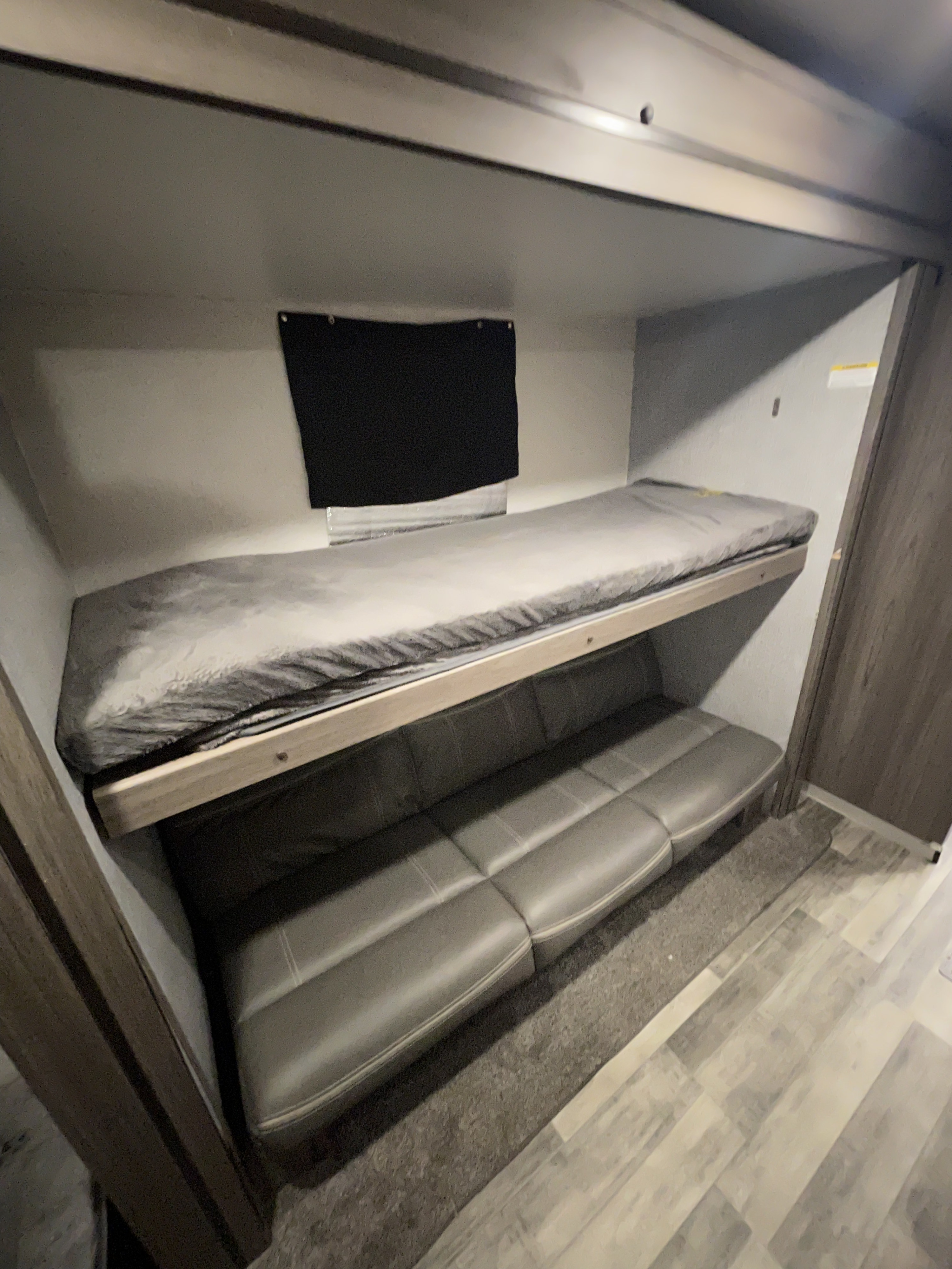 This RV rental's interior shows bunk beds: a grey top mattress and a lower cushioned sofa, ideal for camper sleeping.. Crossroads RV Volante 2021