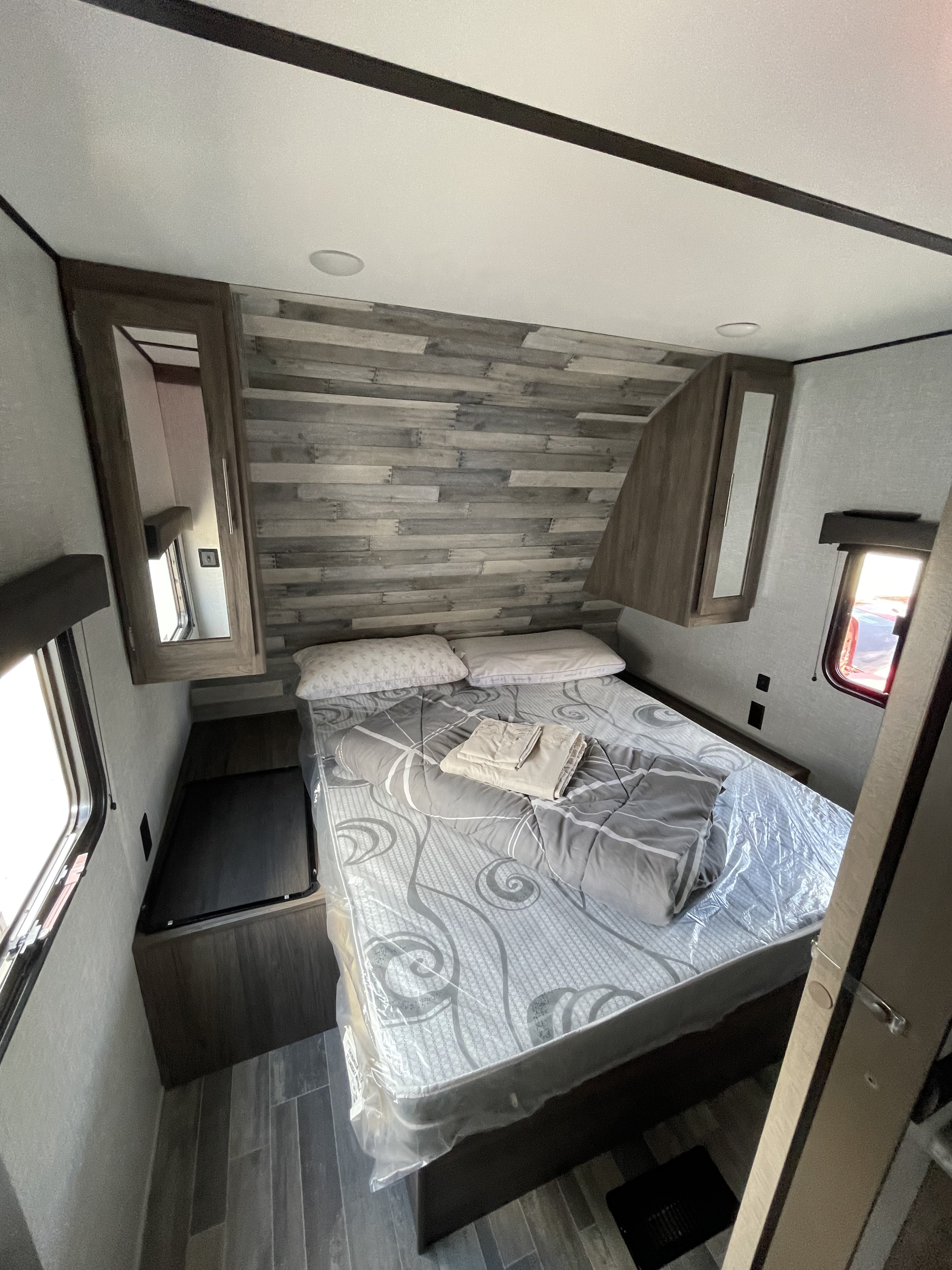 Spacious RV rental bedroom with modern wood paneling, comfortable bed (in plastic), overhead storage, and windows.. Crossroads RV Zinger Lite 2021