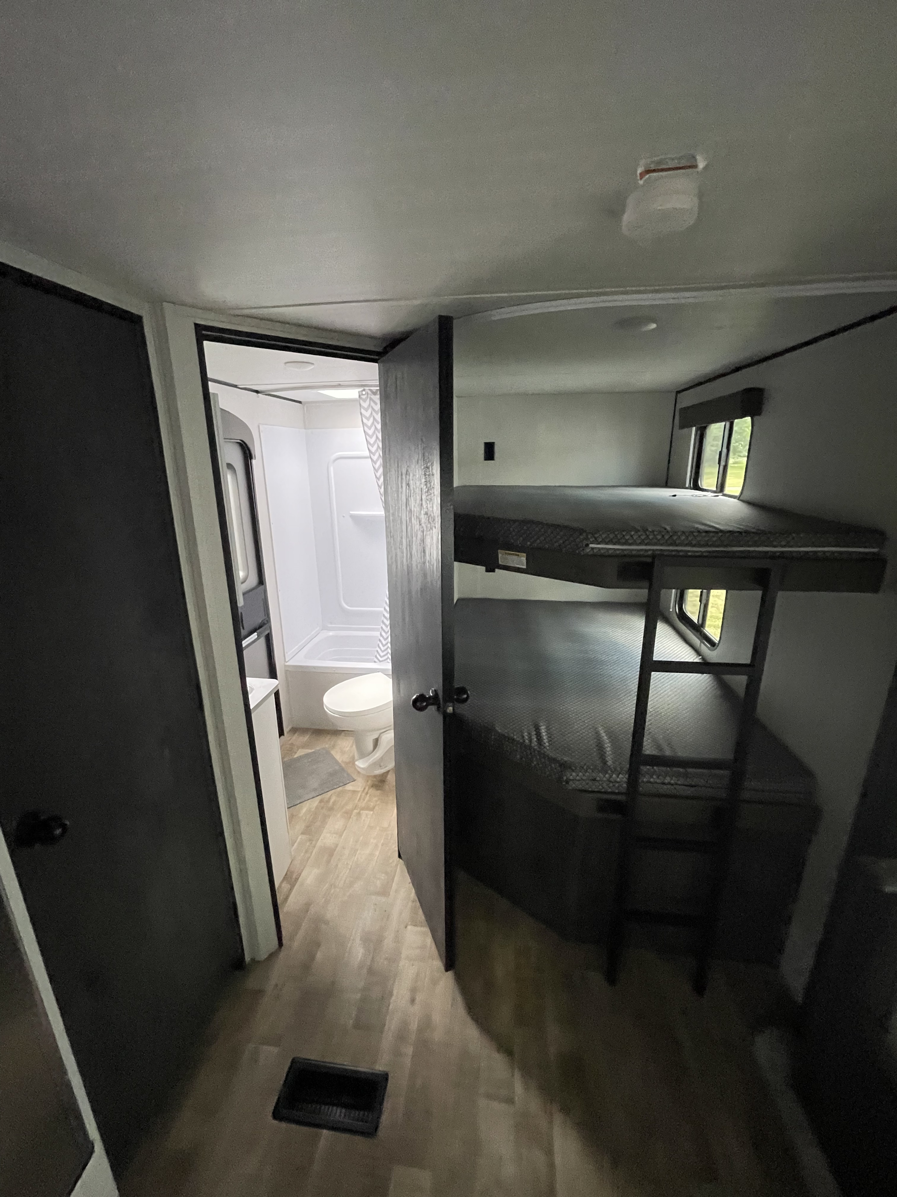 View inside an RV rental showing a light bathroom with toilet and shower/tub on the left, across from dark bunk beds with a ladder.. Keystone RV Hideout 2022