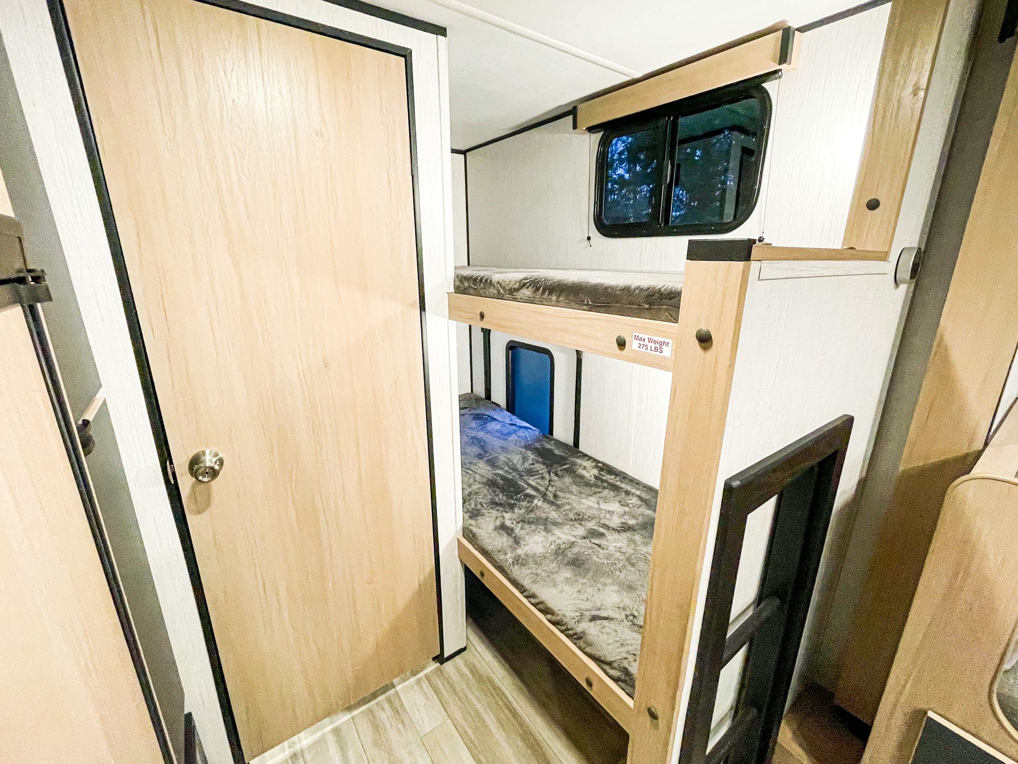 Bright RV rental interior with comfortable bunk beds for travelers. A nearby door and window enhance this sleeping area. Max weight 275 LBS.. Hitch Bunk house 2022