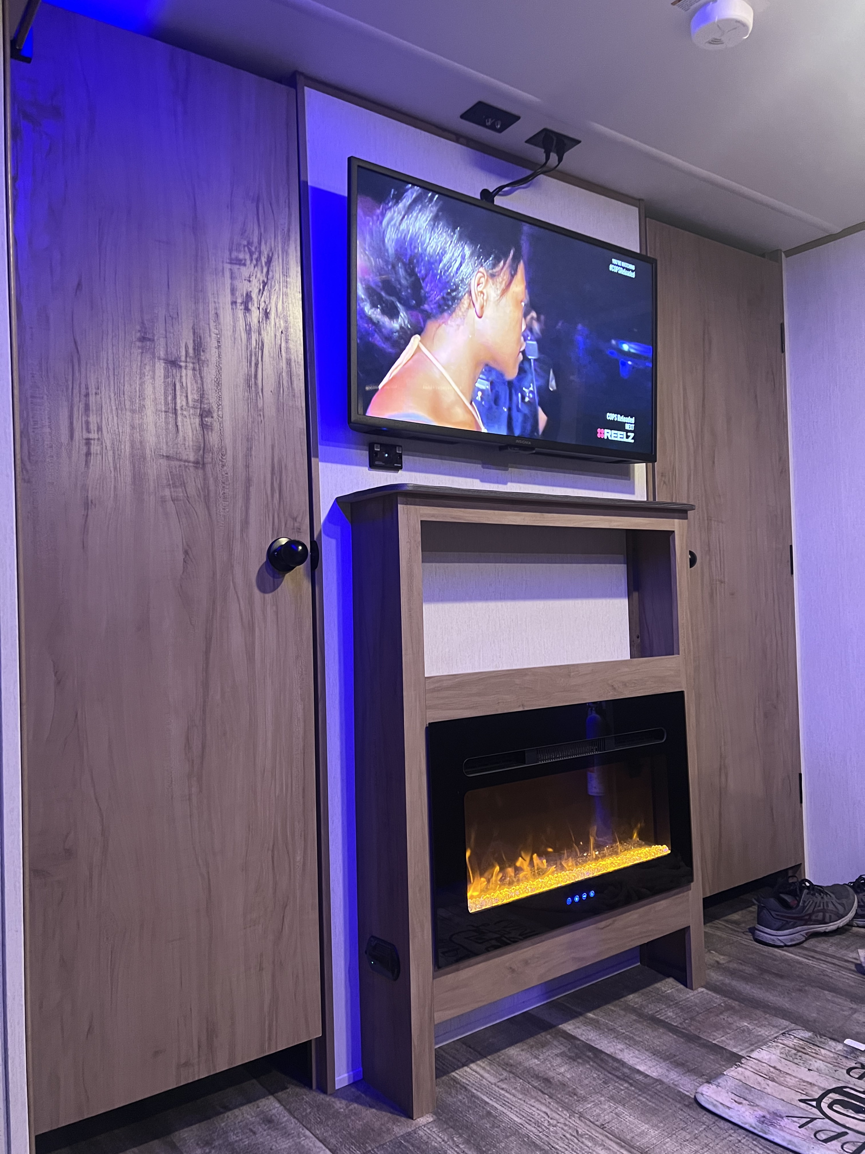 Modern RV rental interior showcasing a mounted TV, electric fireplace, and integrated storage, with ambient blue lighting.. Forest River Cherokee 26 dbh-l 2023