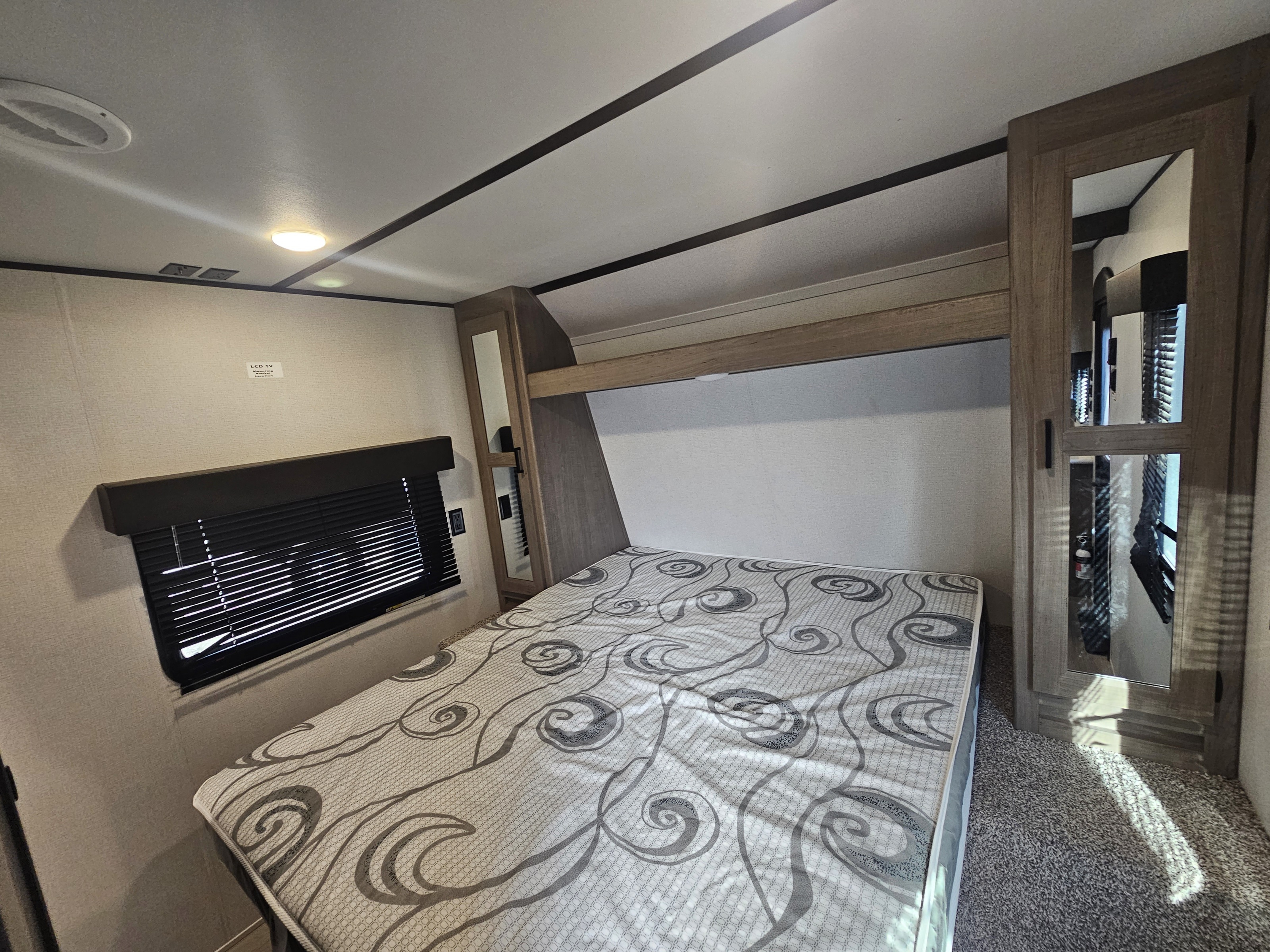 This RV rental bedroom features a comfortable bed, window with blinds, and mirrored wardrobe, providing a functional sleeping space.. Keystone Hideout 2020