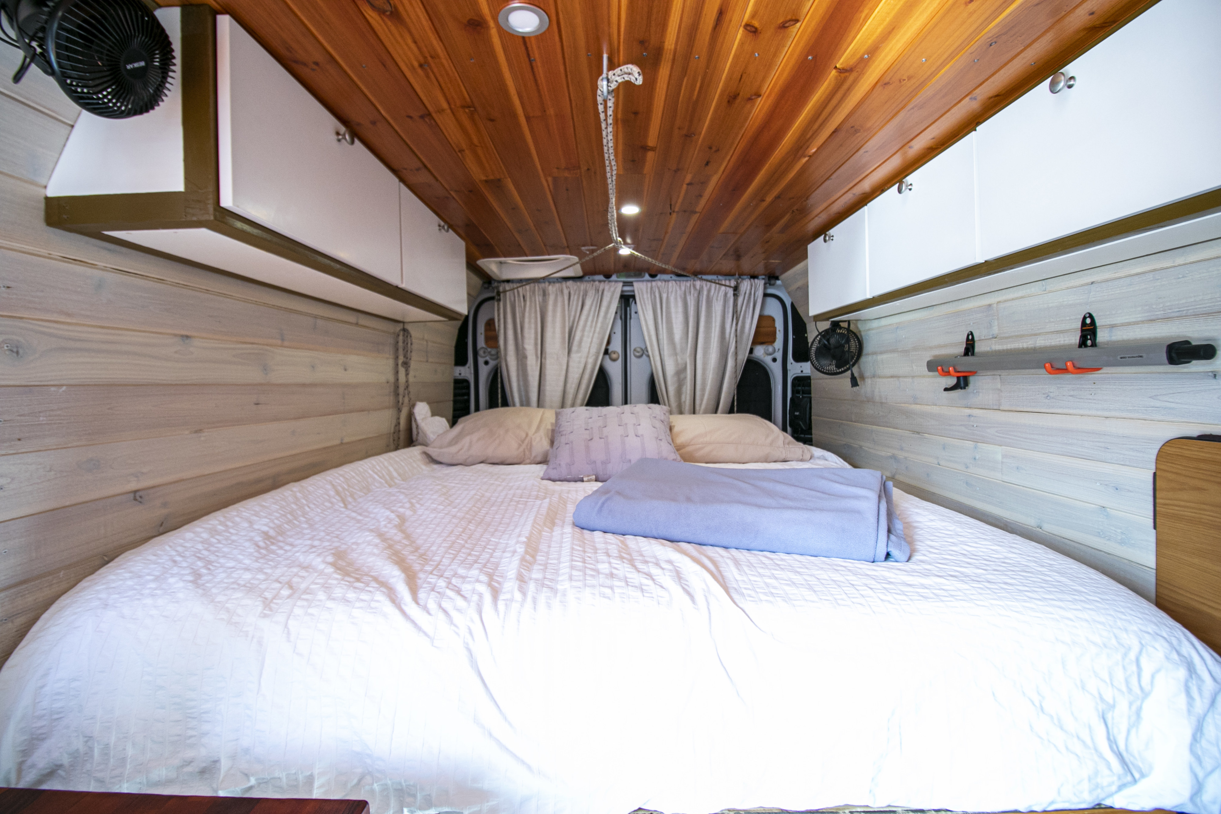 Inside an RV rental: a cozy bed, wood paneling, overhead storage, and fans for a comfortable travel experience.. RAM Promaster 3500 2020