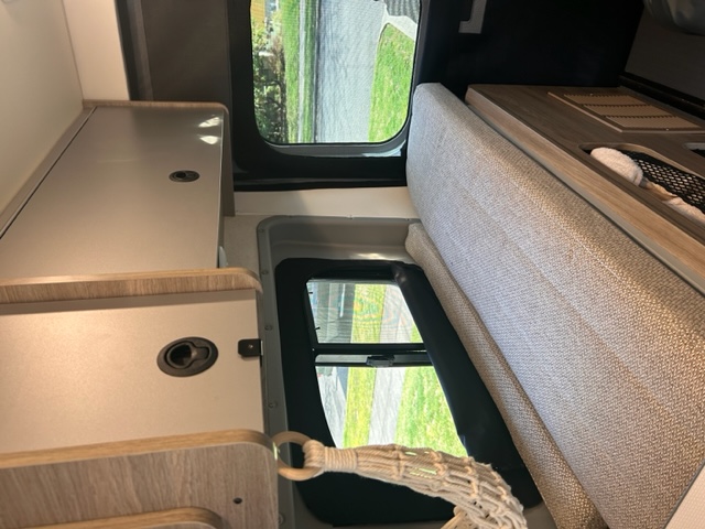 Compact rv rental interior showing light wood cabinets, textured seating, and exterior views through windows.. Winnebago Solis 59P 2022