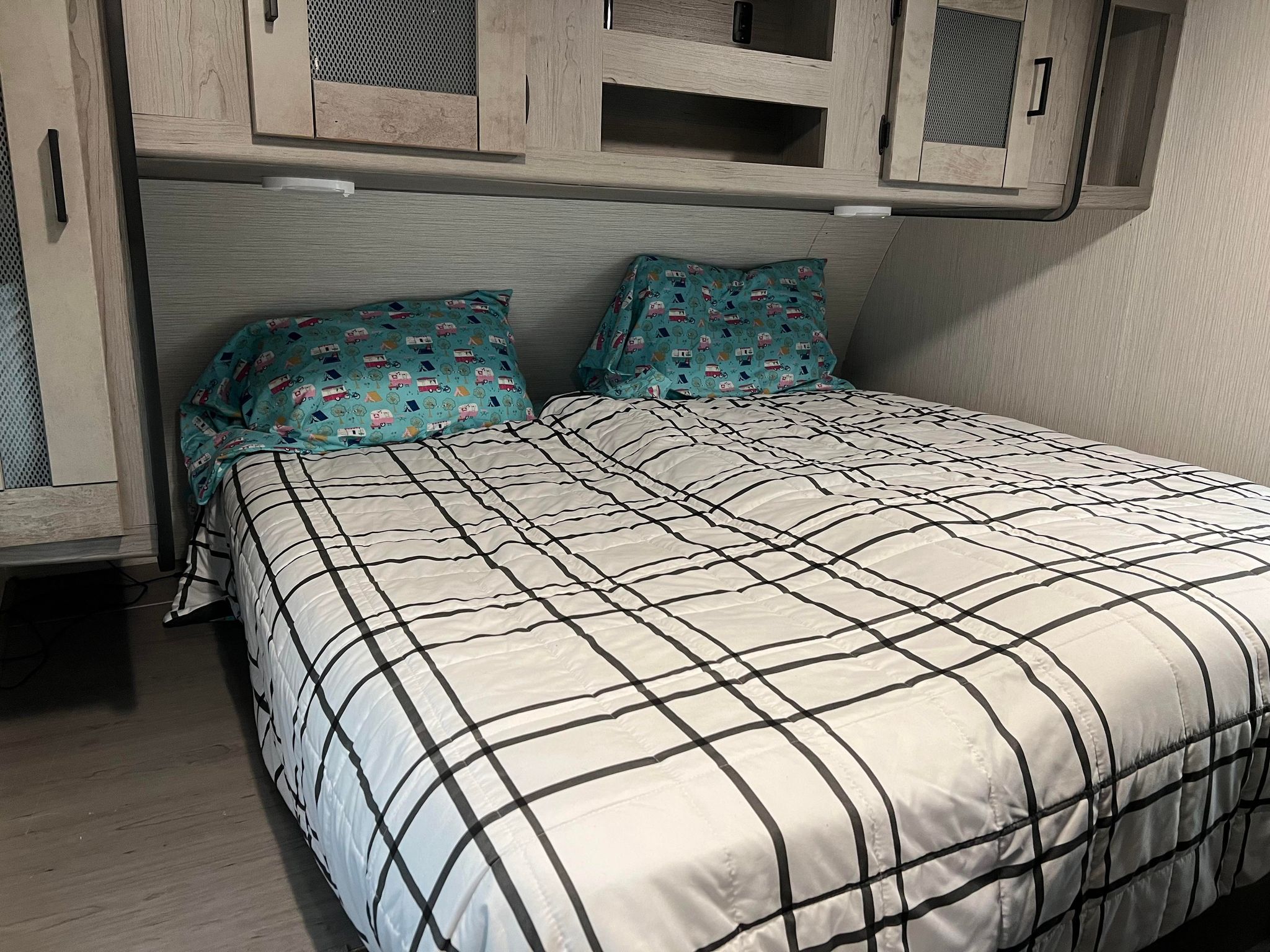 Cozy RV rental bedroom with patterned pillows, plaid comforter, and overhead storage.. Heartland RVs Mallard 2021