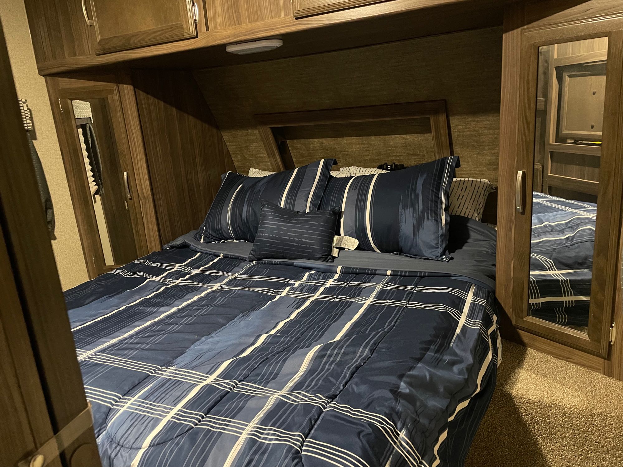 Cozy RV rental bedroom featuring a blue striped bed, built-in wood cabinets, and mirrored closets.. Coachmen Apex 2017