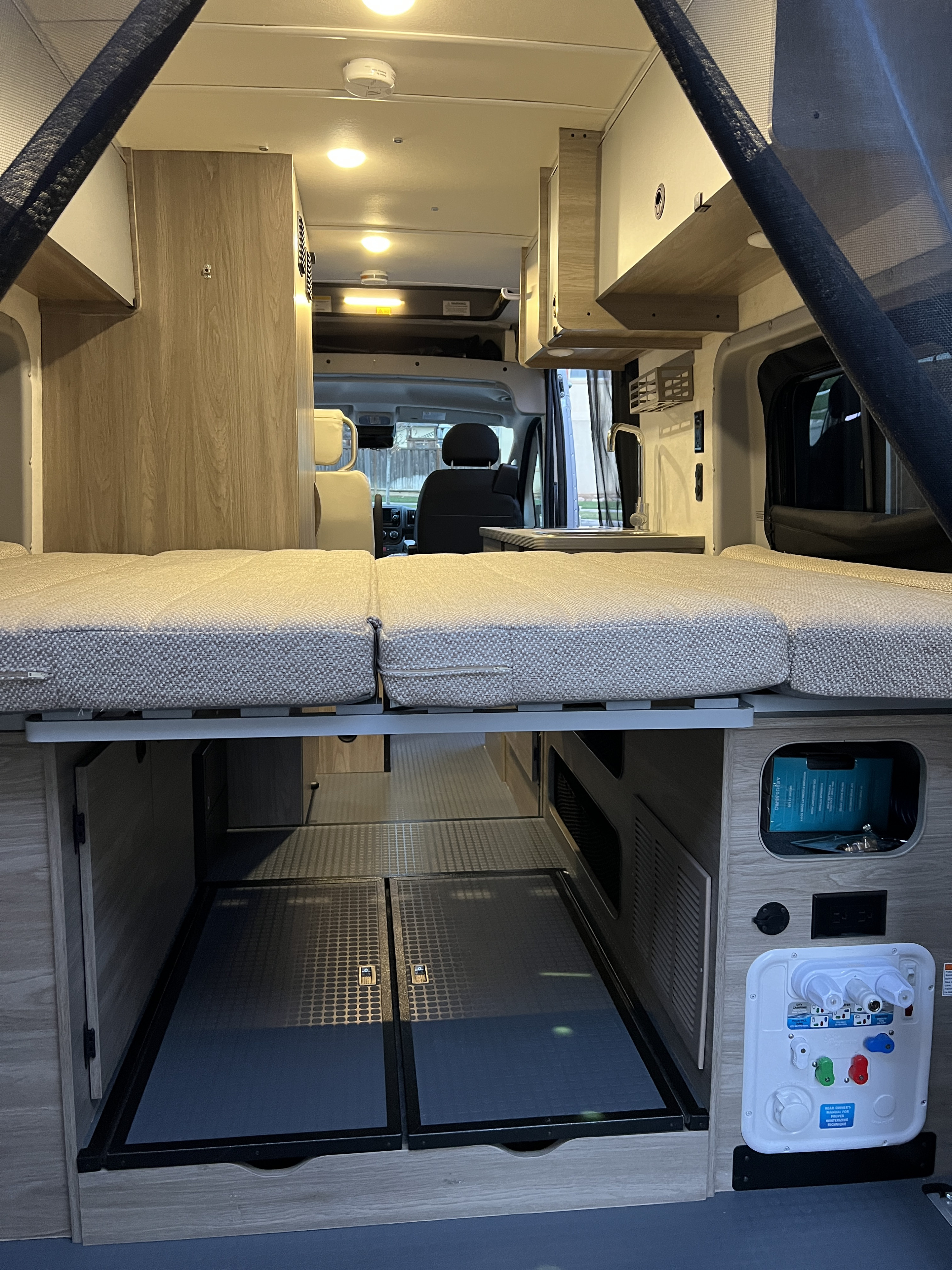 Inside an RV rental: view of the bed, under-bed storage, and utility panel in a camper van. Designed for travel comfort.. Winnebago Solis 2022