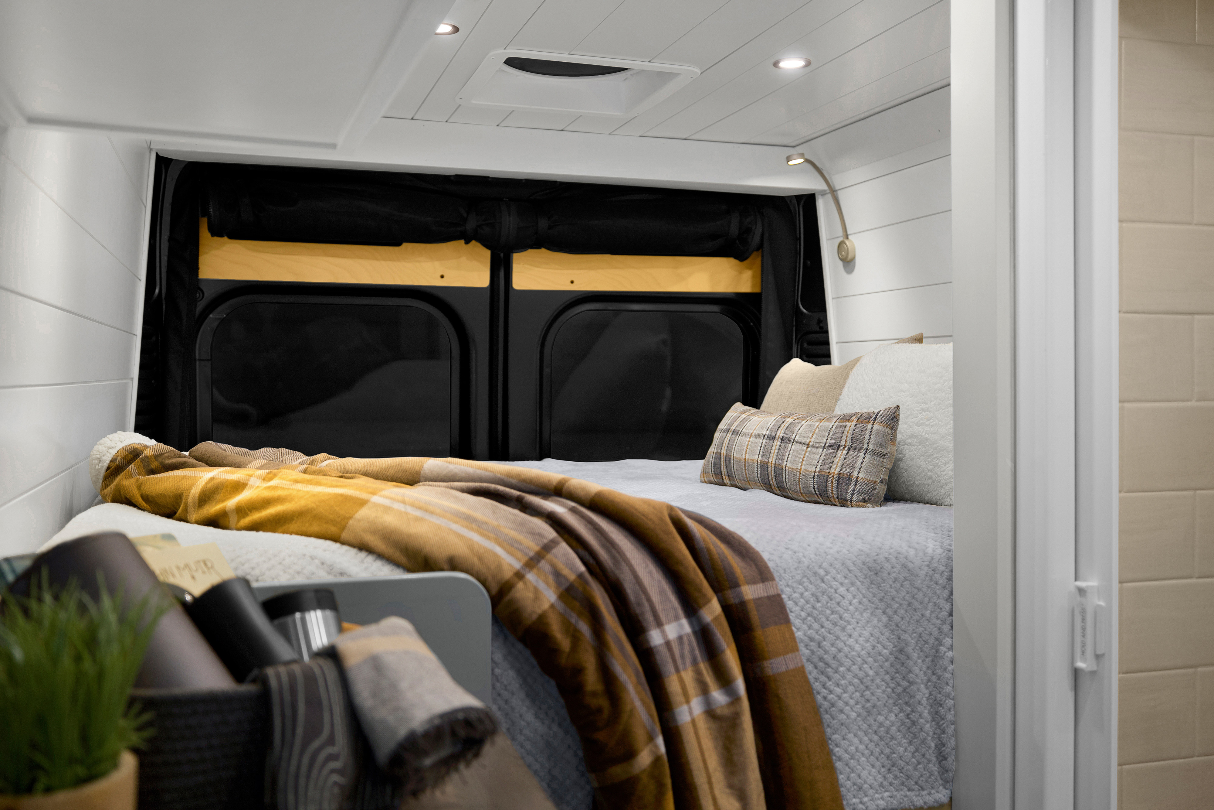 Cozy RV rental bedroom: white shiplap walls, comfy bed with plaid blanket, and smart built-in lighting.. Ram ProMaster 2021