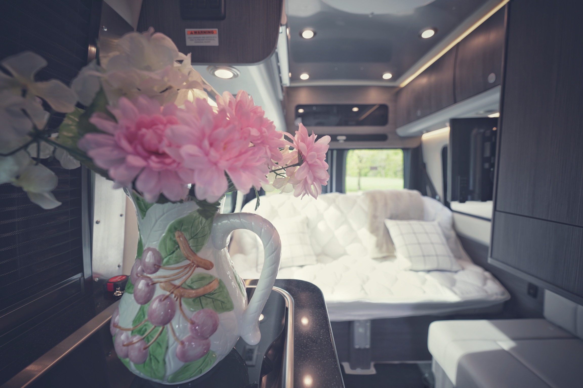 This inviting RV rental interior features a cozy bedroom, kitchenette with flowers, and modern amenities, ready for your next adventure.. Airstream Interstate 2022