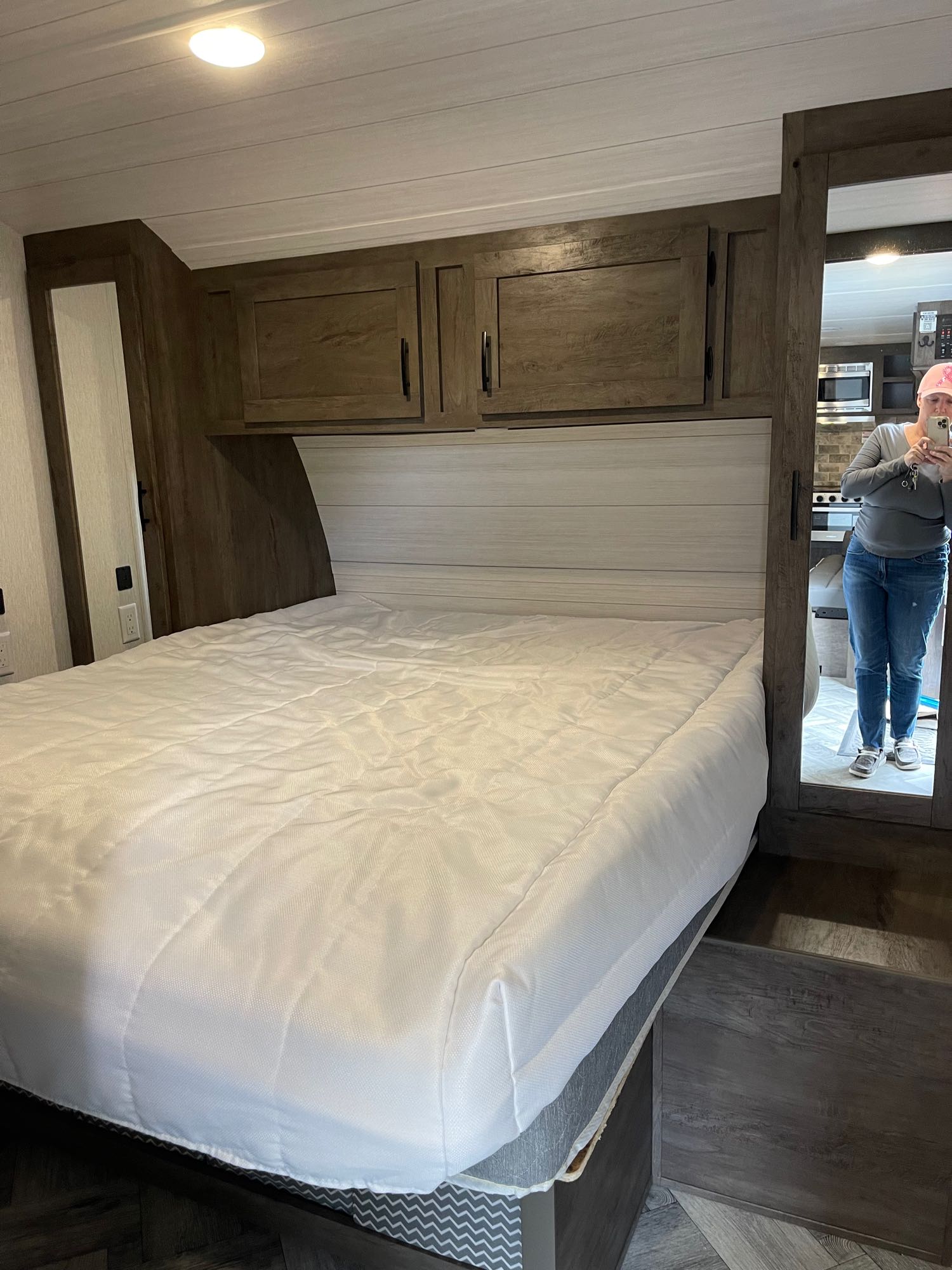 This RV rental bedroom features a cozy interior with a white-covered bed, overhead cabinets, and a mirrored view of the kitchen.. Forest River Evo 2022