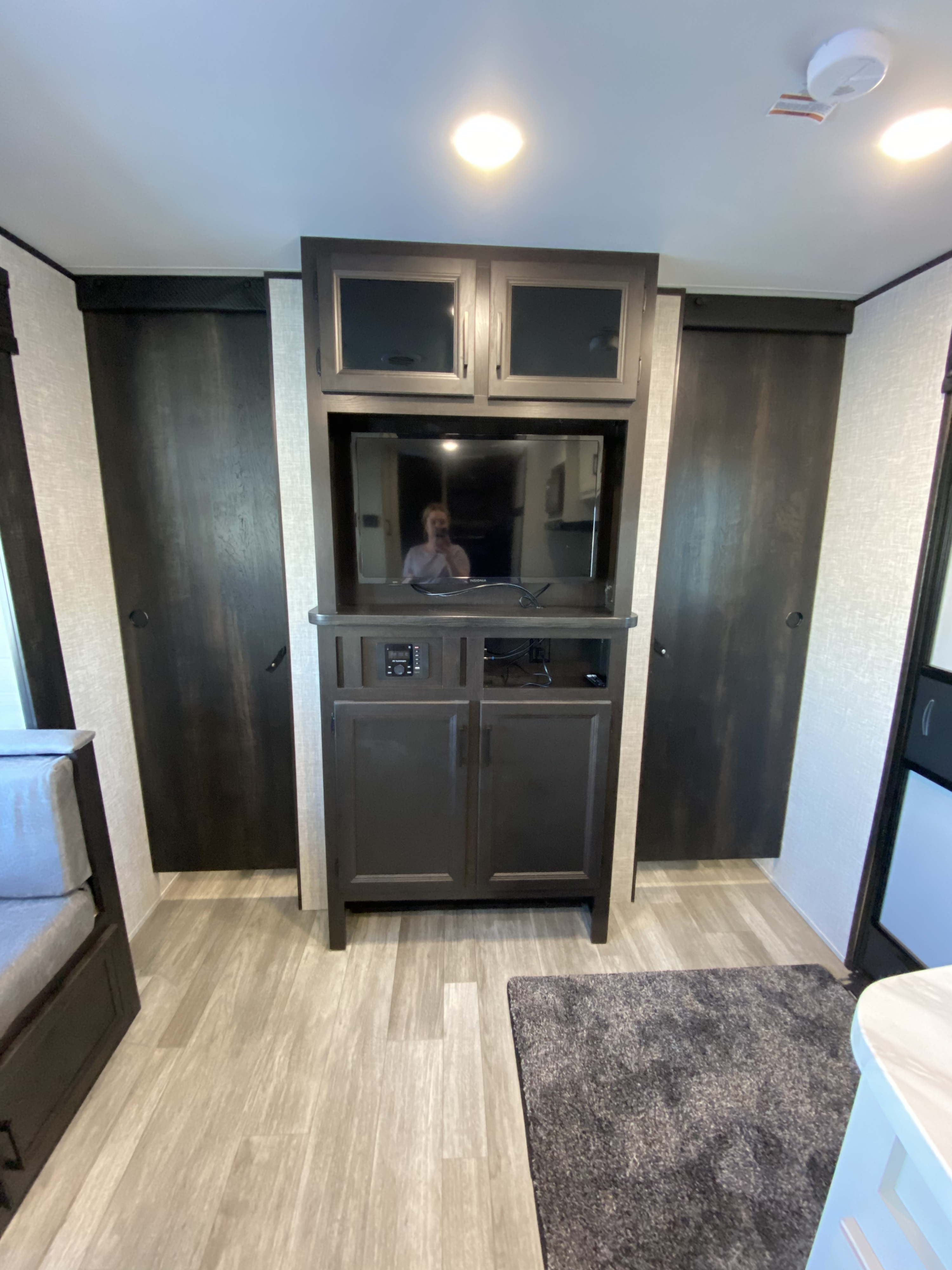 RV rental interior: modern entertainment center with TV, dark cabinets, flanking closets, and light wood-look floor.. JAYFLIGHT 242BHSW-G 2023
