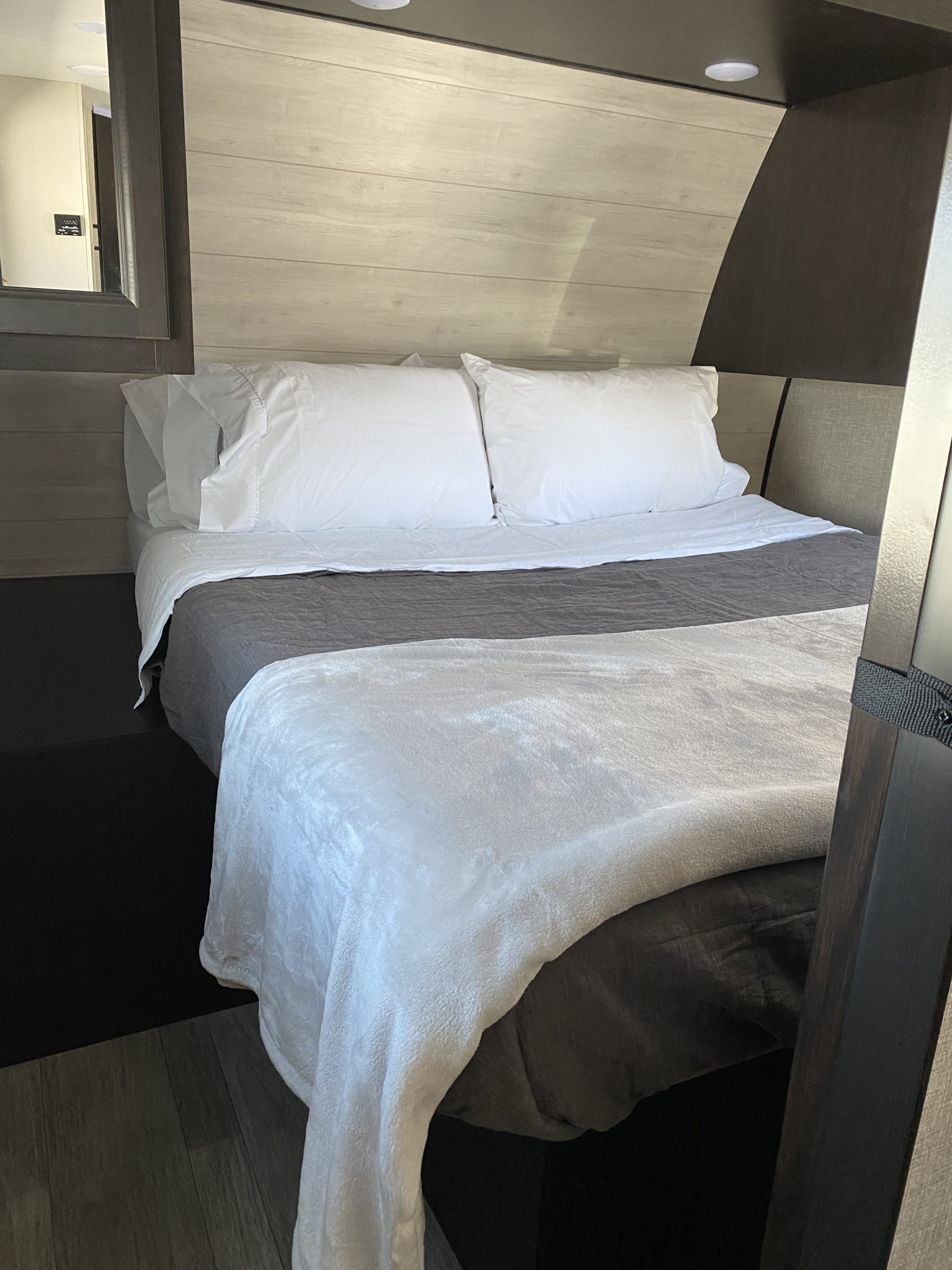 This cozy RV rental sleeping area features a neatly made bed with white linens & a plush blanket, set against wood-paneled walls.. JAYFLIGHT 242BHSW-G 2023