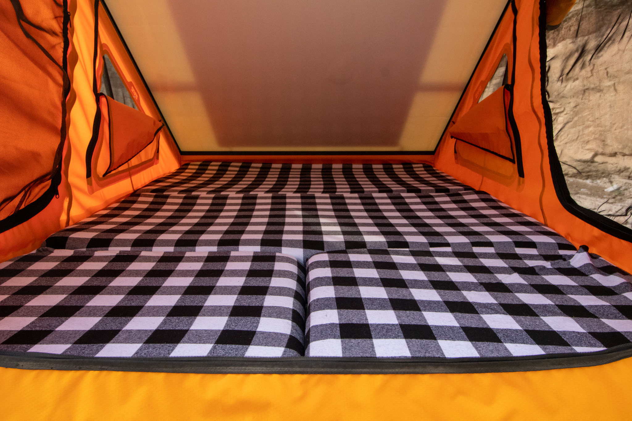 Cozy interior of an RV rental's rooftop tent, featuring a comfy black and white checkered mattress and orange walls.. Ram Power Wagon 2022