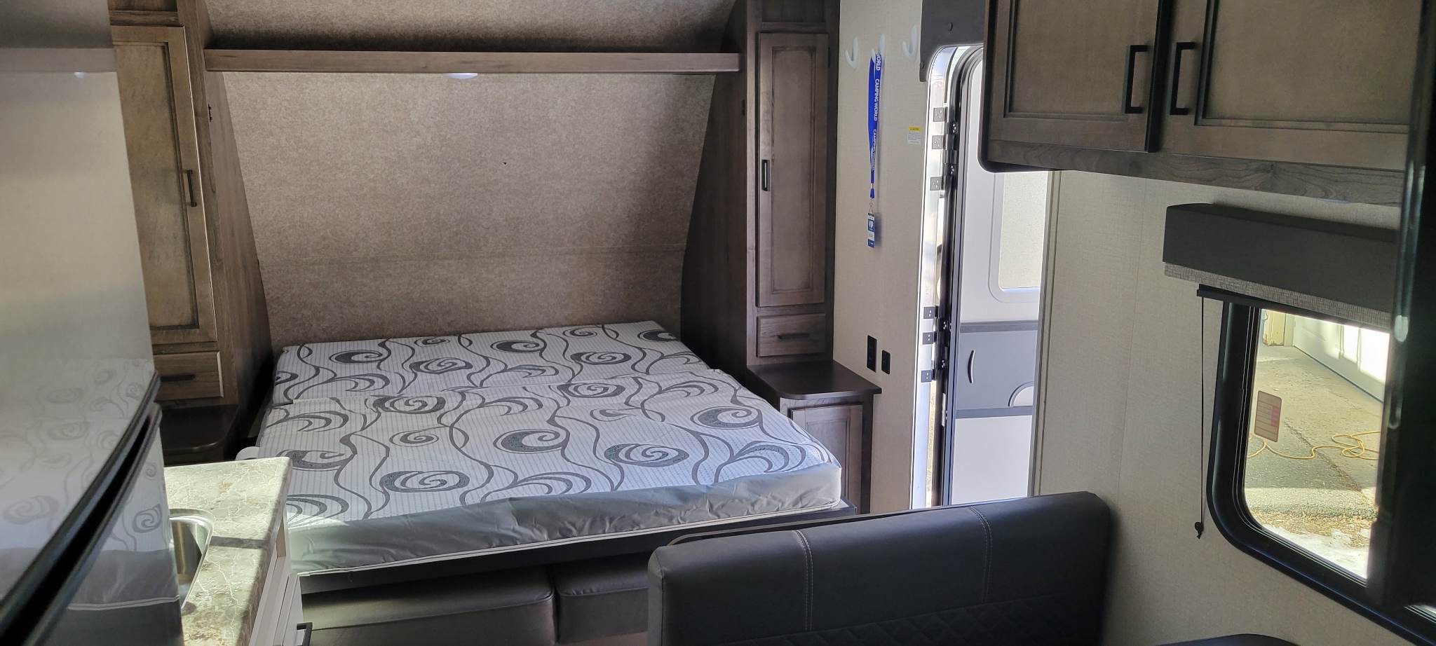 Inside an RV rental: a compact interior with a fold-down bed, kitchen area, storage cabinets, and open main door, ideal for travel.. Highland Ridge RV Open Range 2021