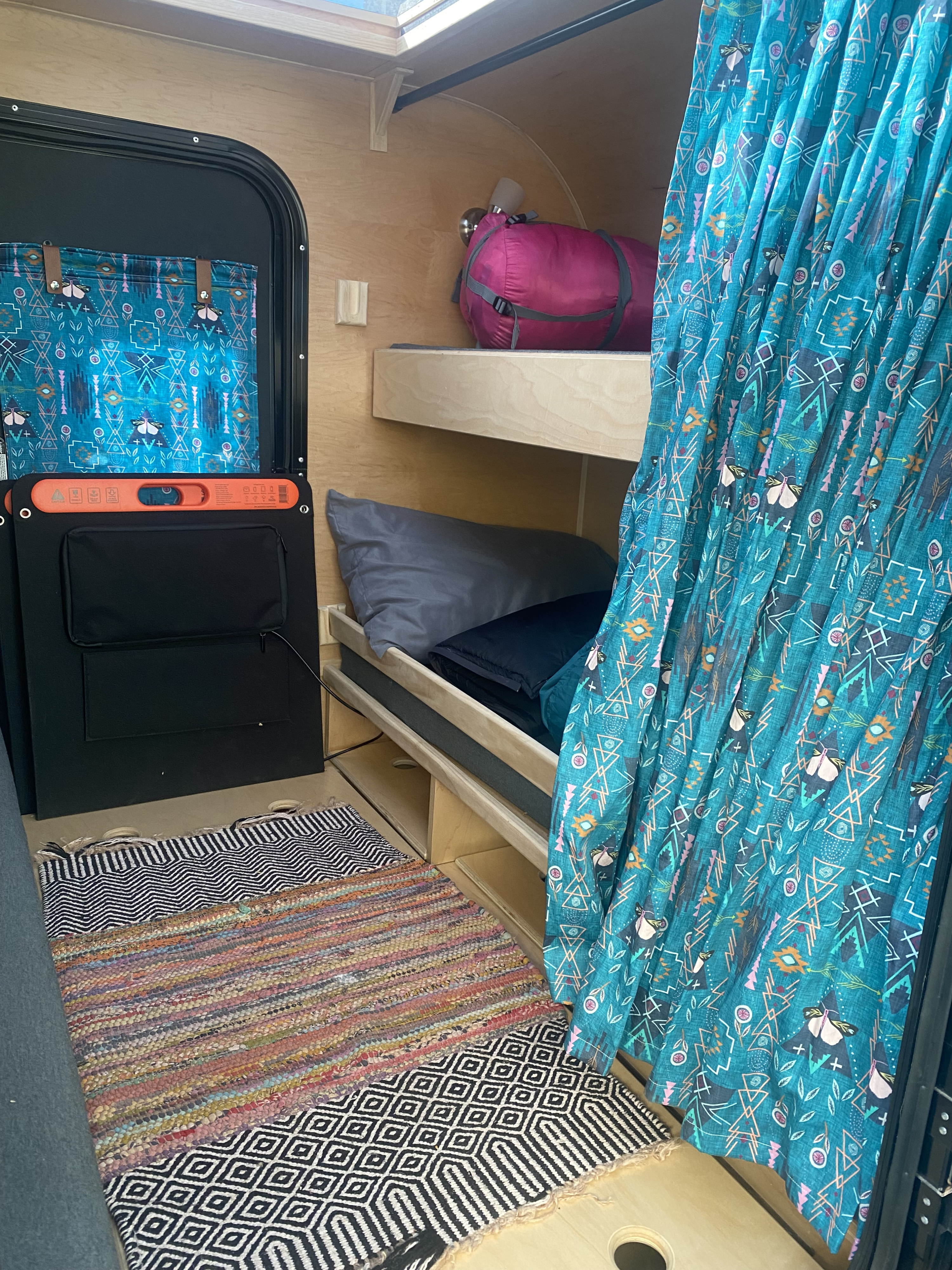 Inside a comfy RV rental: bunk beds, patterned teal curtains, and vibrant floor rugs. A cozy camper space.. Colorado Colorado Trailer 2022