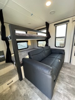 Explore this spacious RV rental interior, featuring a comfy black sofa and sturdy bunk beds for family comfort.. Coachmen 266 BHS 2023