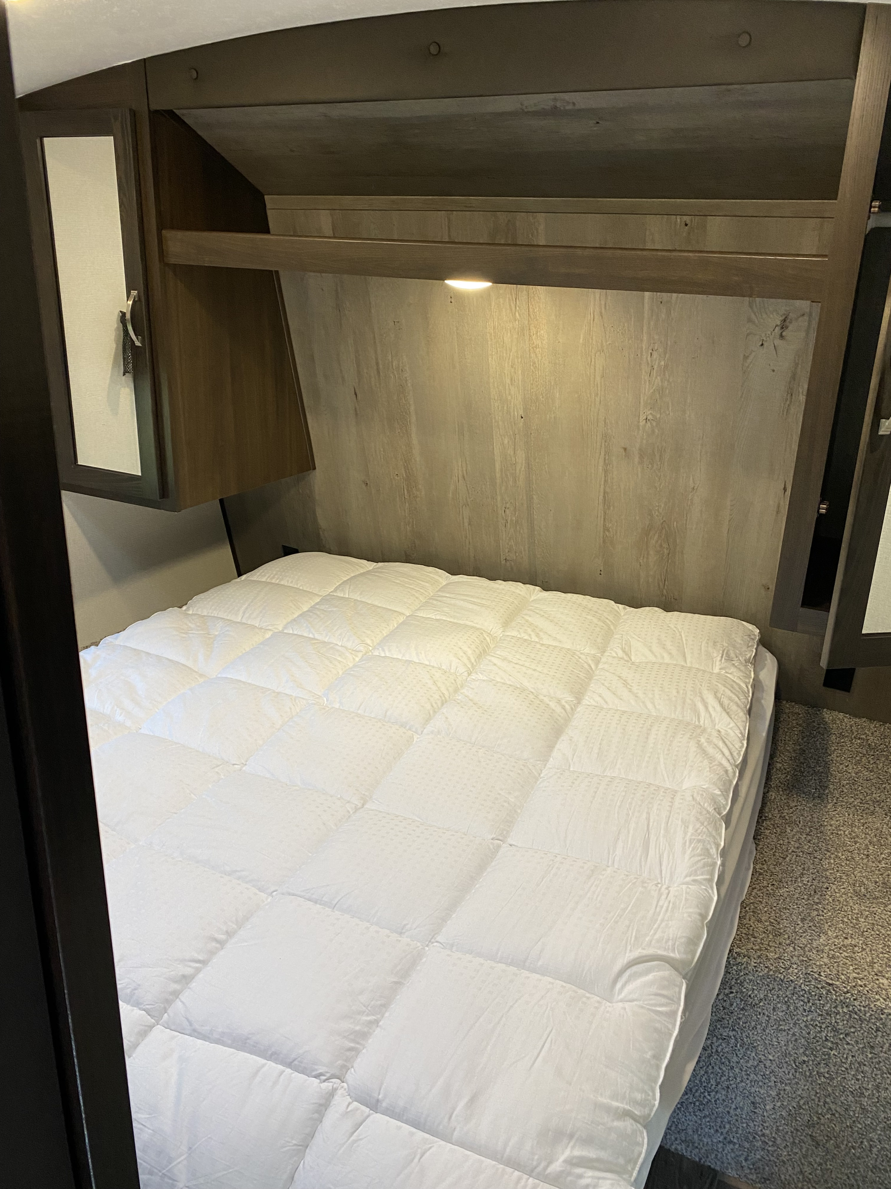 Step into this comfortable RV rental bedroom, featuring a plush bed, overhead cabinets, and warm lighting.. Keystone RV Springdale 2021