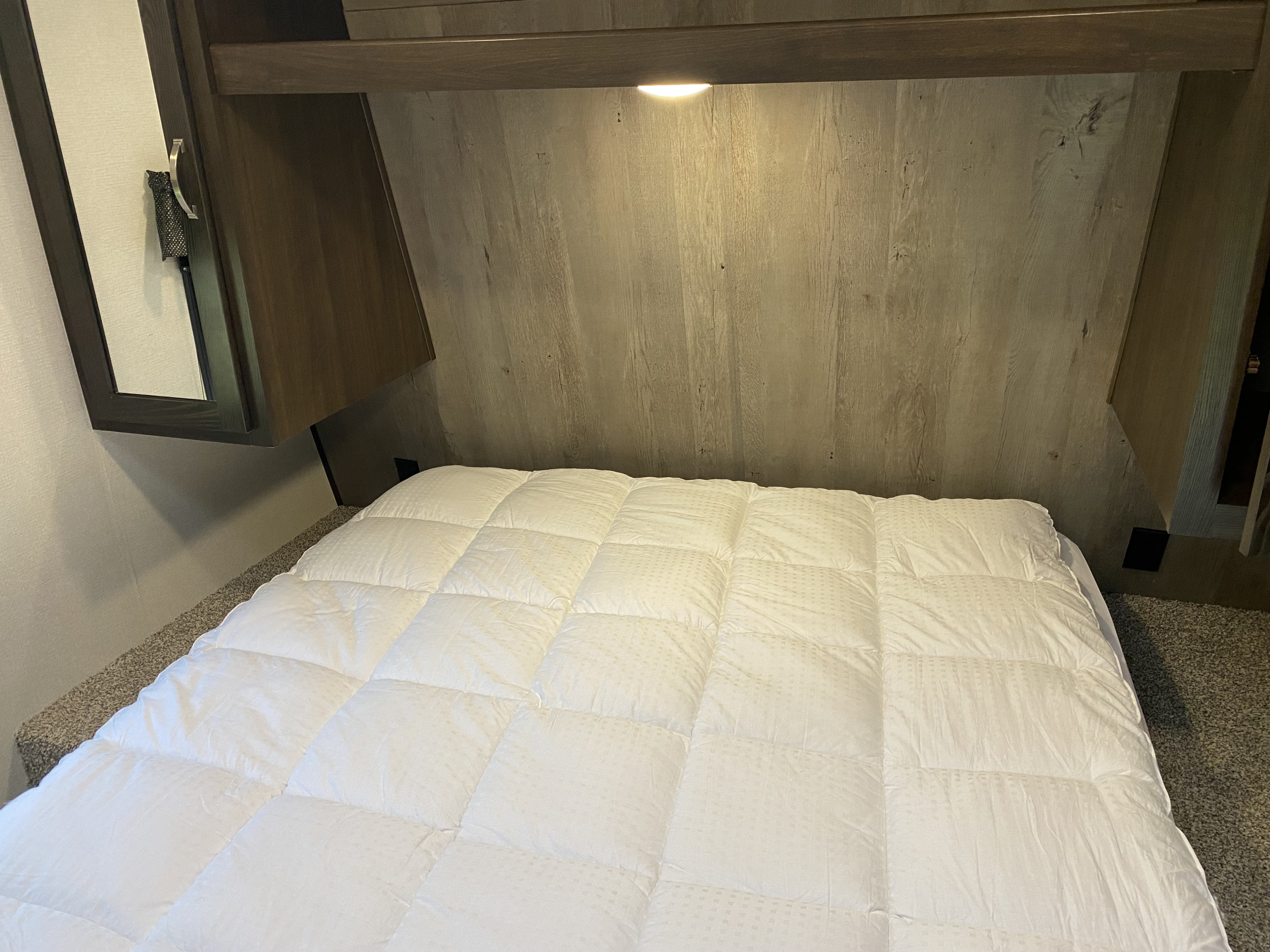 Cozy RV rental bedroom featuring a white quilted comforter, wooden headboard with built-in light, and dark cabinets.. Keystone RV Springdale 2021