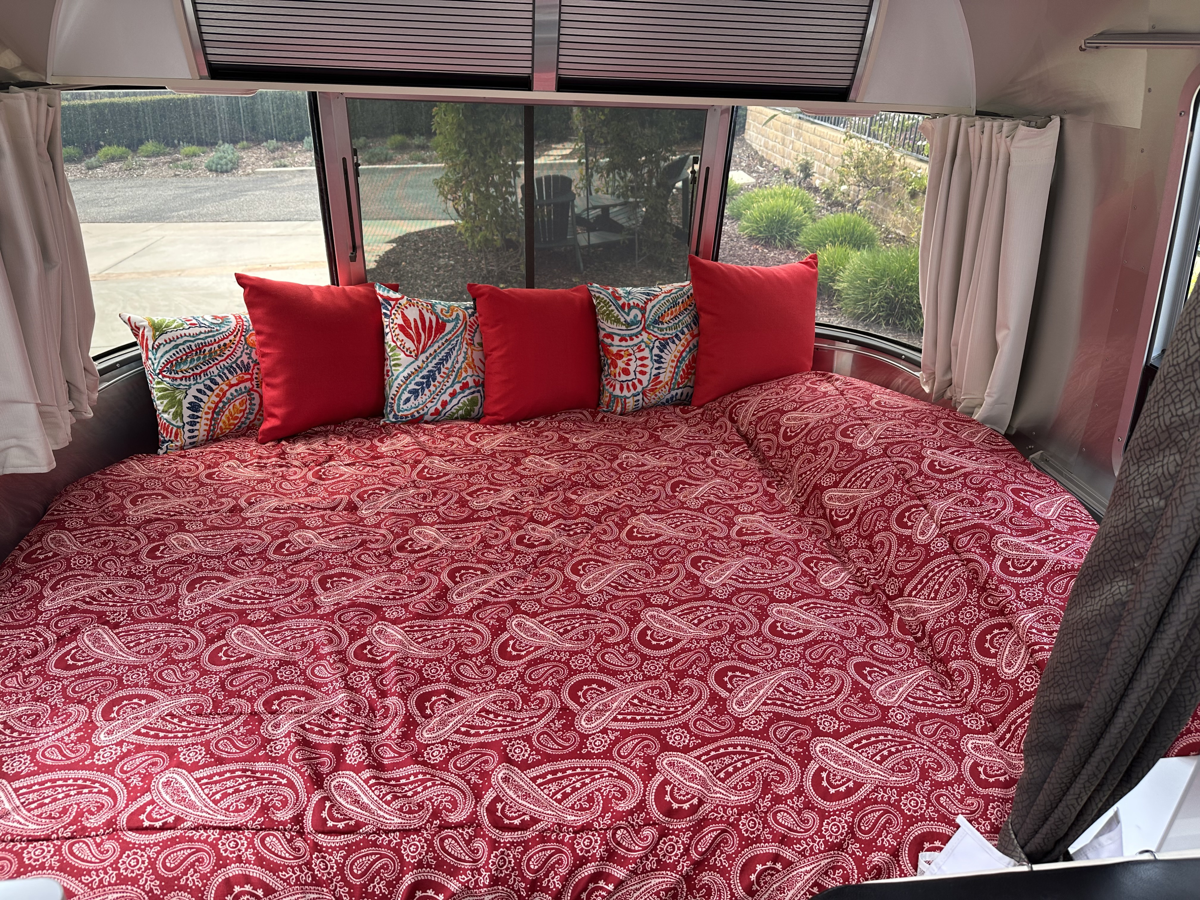 Cozy RV rental bed featuring a red paisley comforter & vibrant pillows, ready for restful nights.. Airstream Sport 2018