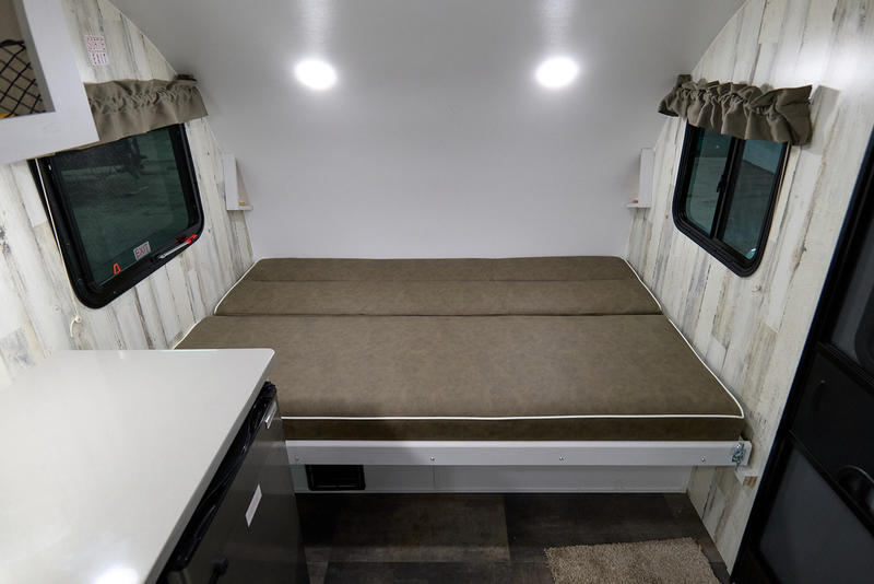 RV rental interior: cozy bed, side windows, and compact counter with fridge. Perfect for your next adventure.. Travel Lite Rove Lite 2023