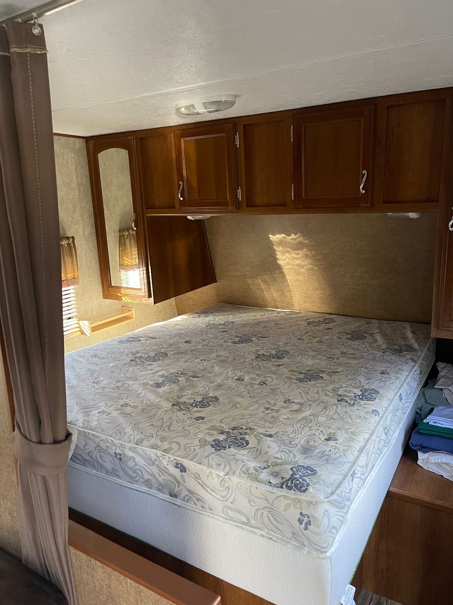 Comfortable RV rental bedroom with a floral bed, wooden cabinets, and a mirror. Ideal for your next adventure.. Avenger Avenger Trailer 2015