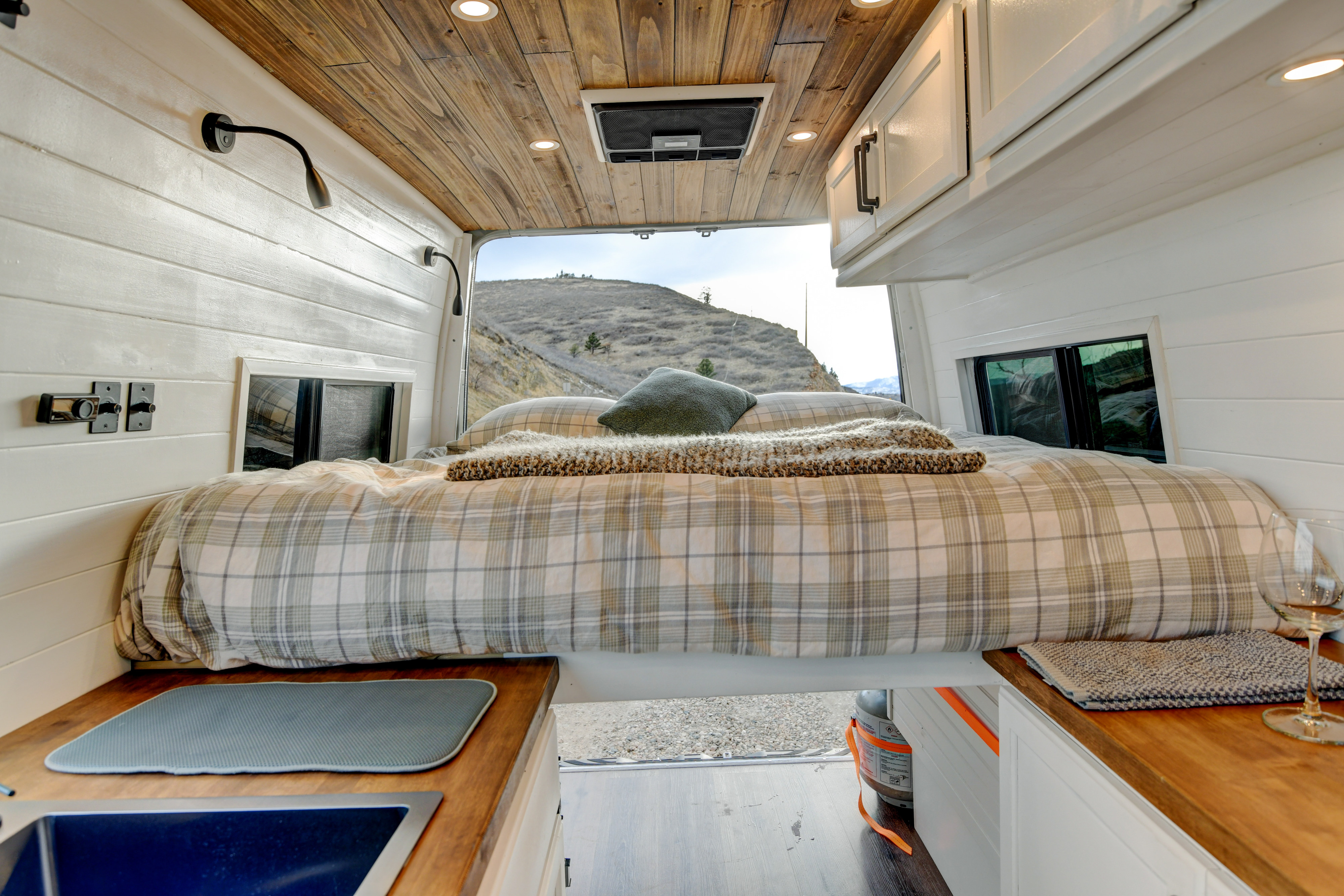 Inside an **rv rental** van: Plaid bed, wood ceiling, kitchenette, and mountain view from the open back.. Mercedes-Benz Sprinter 2026