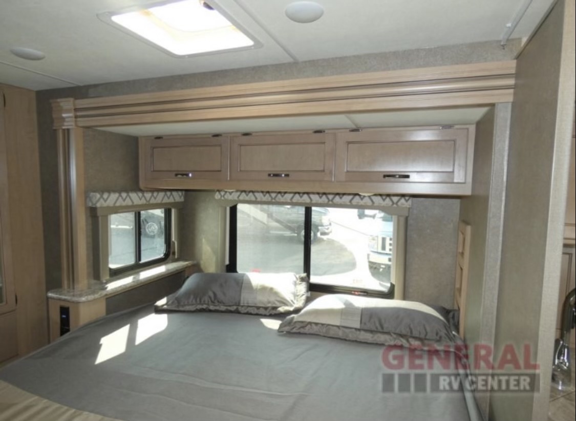 This RV rental bedroom features a comfortable bed, overhead storage, and natural light from windows and a skylight.. Thor Quantum 2020